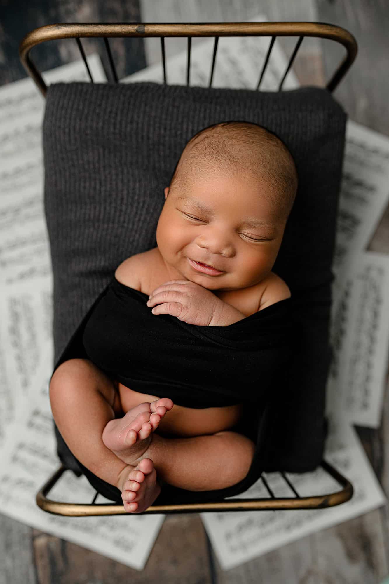 5 week old newborn boy wrapped in a black wrap smiling 