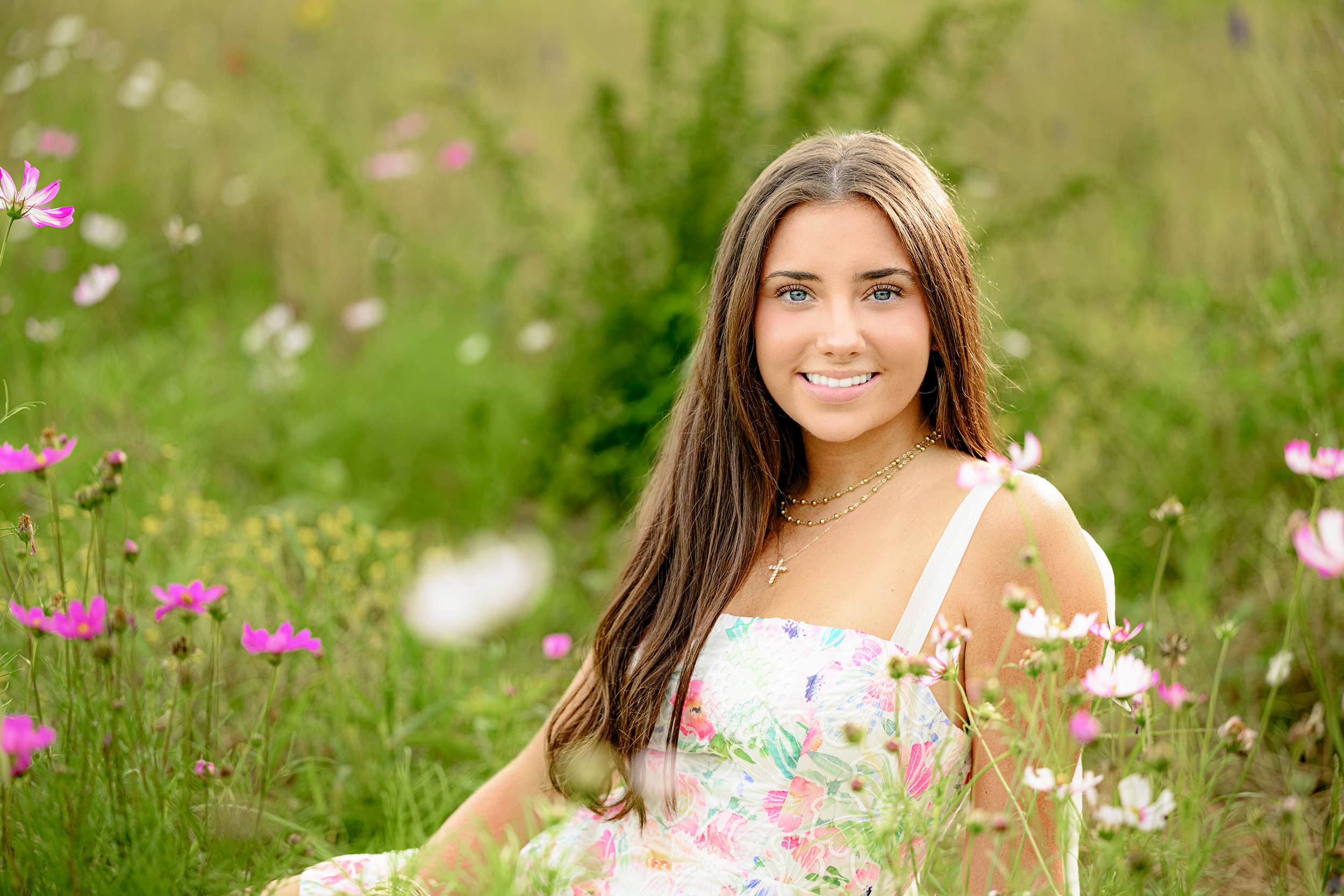 graduate sitting in field with floral dress with professional hair and makeup completing her look