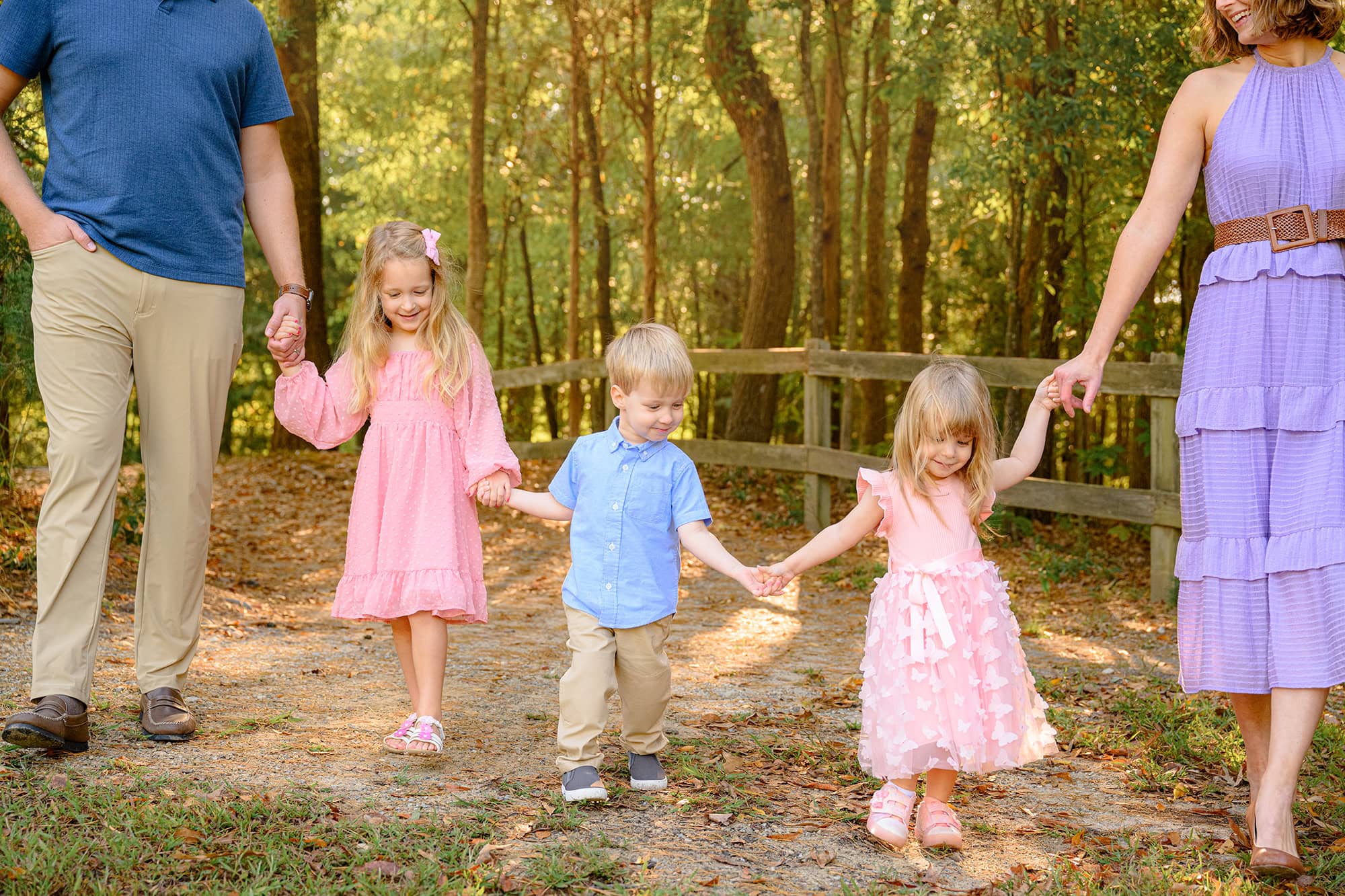 three sibling holding each others hands while walking with their parents in a charlotte park
