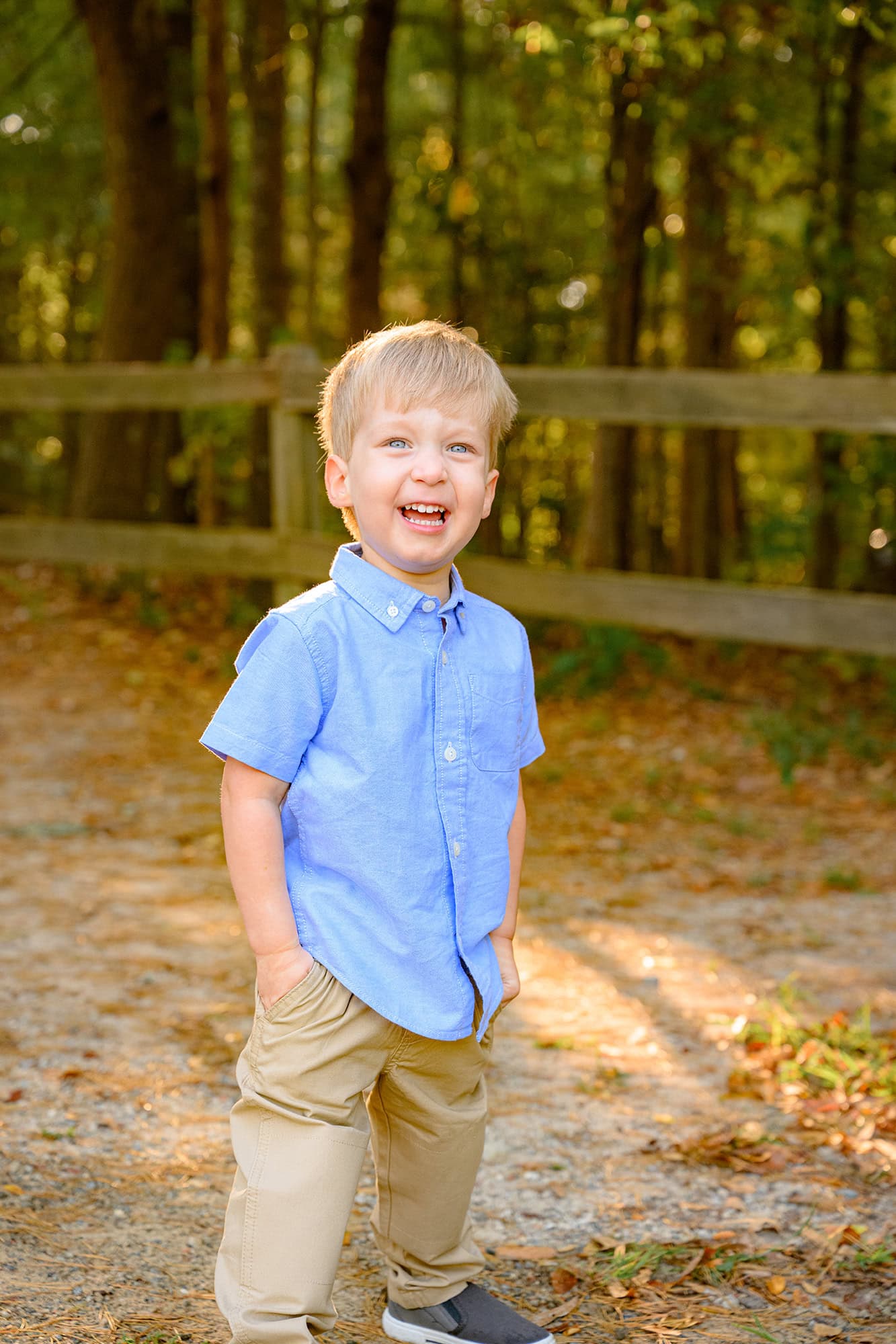 little boy standing in a blue shirt in a waxhaw park laughing with his hands in his pockets