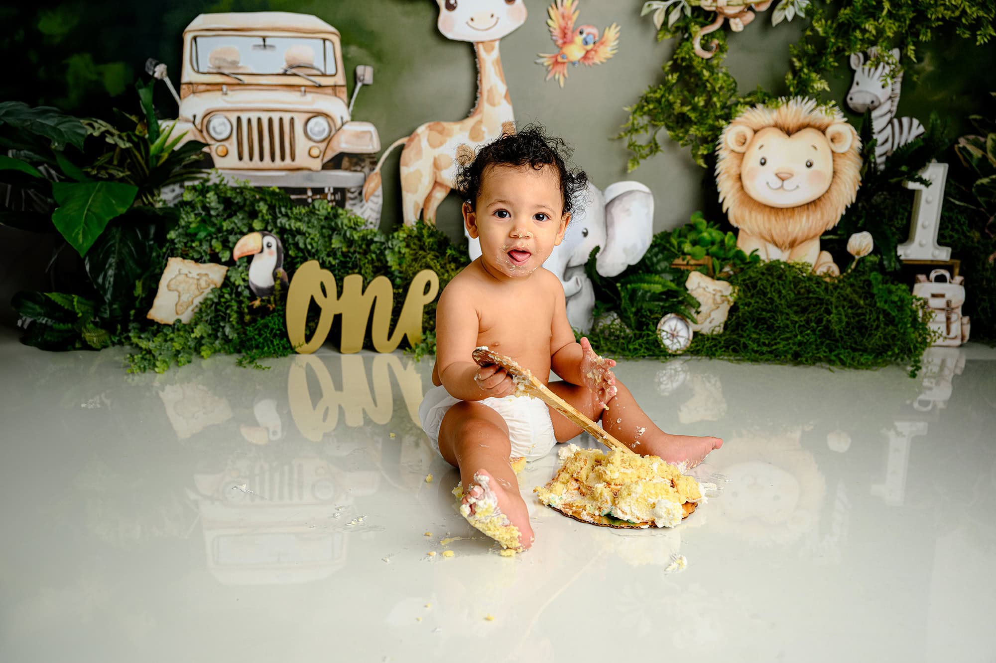 cake smash messes surround this little one year old during his first birthday session