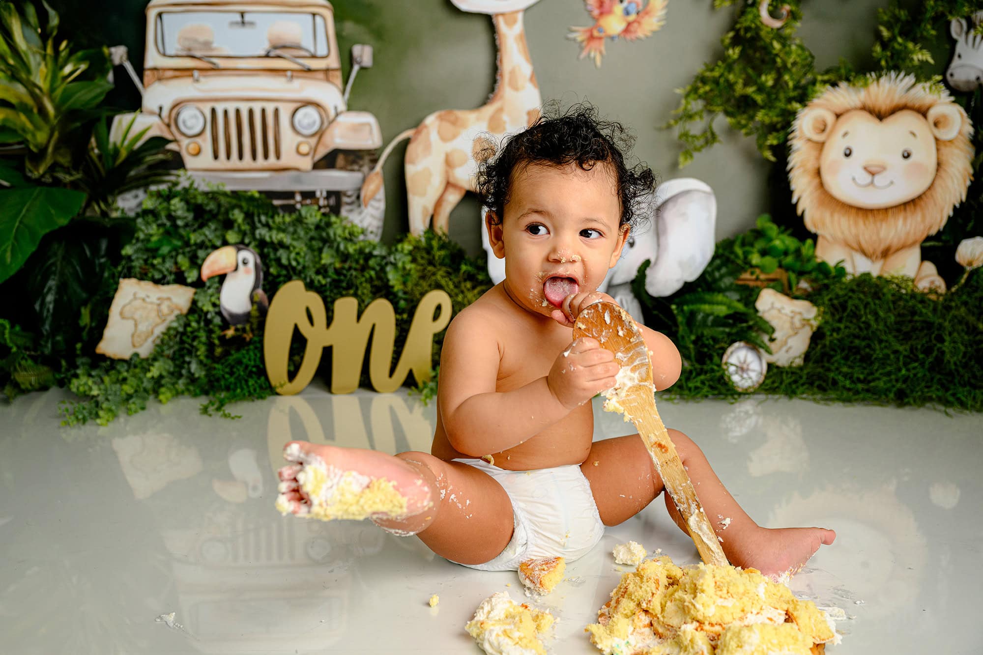 little charlotte one year old boy holds his cake covered foot out after getting icing all over during his cake smash