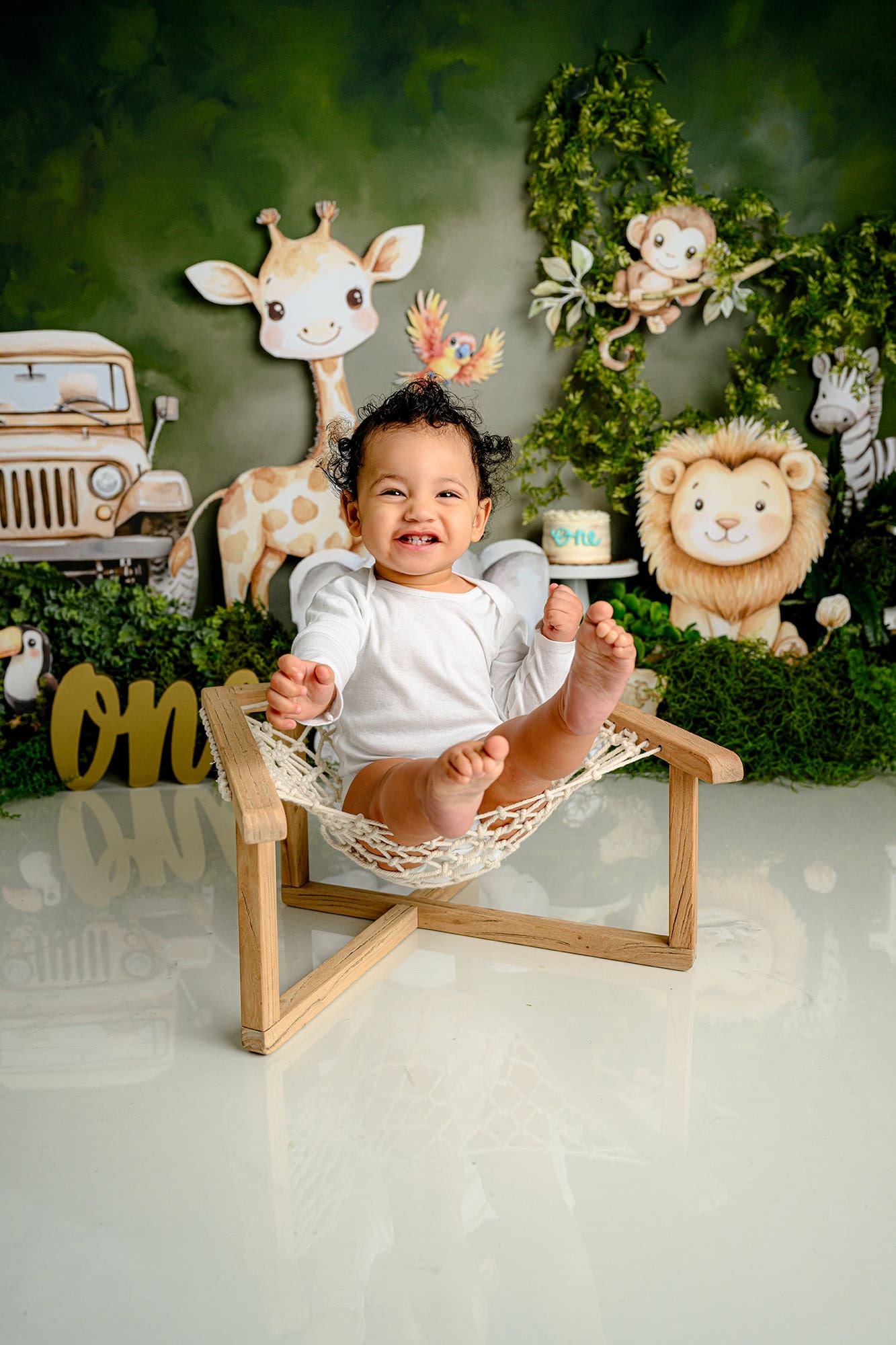 one year old boy laughs as he sits in a web seat during his wild one themed cake smash