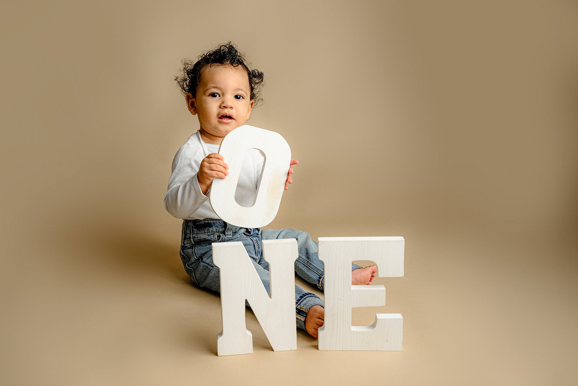 charlotte one year old boy sits holding the O in the ONE wooden letter set during his birthday photos