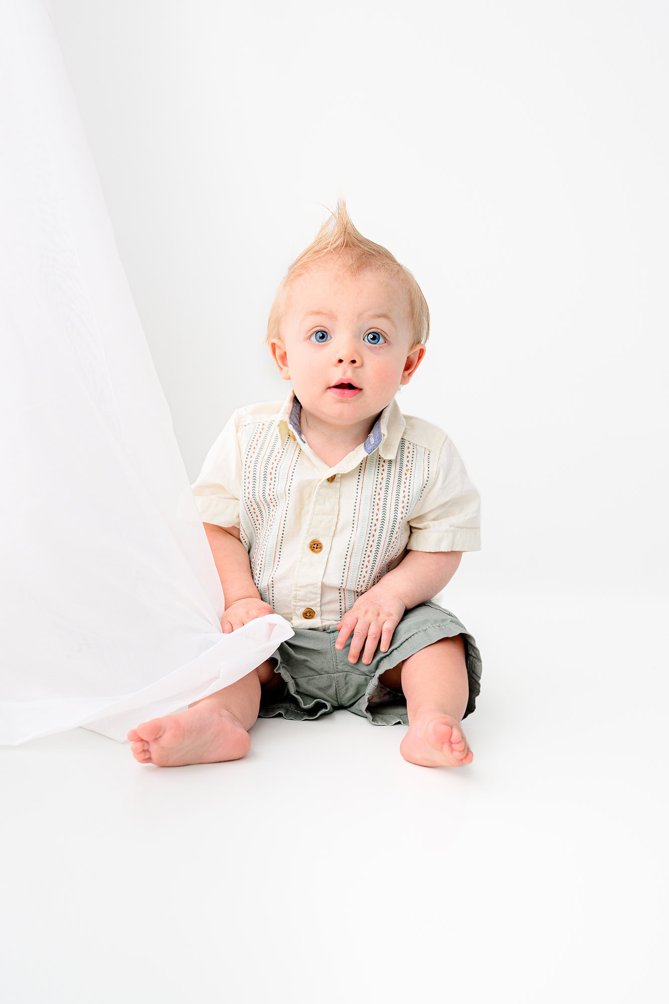 little boy who attends a local waxhaw preschool sits in a studio photo session wearing green shorts and a cream top