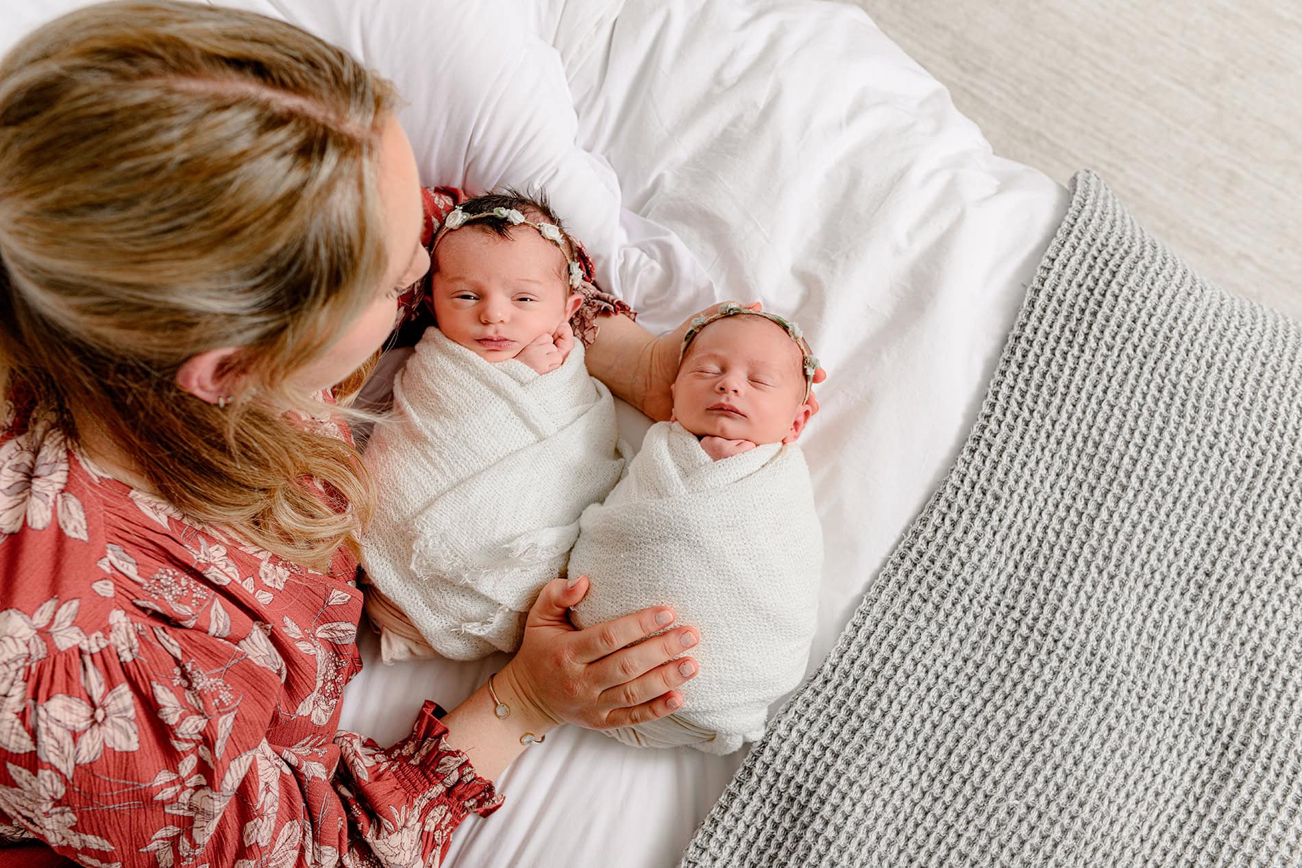 mothre wearing a floral dress looking down on her twin newborn daughters during her charlotte newborn lifestyle session