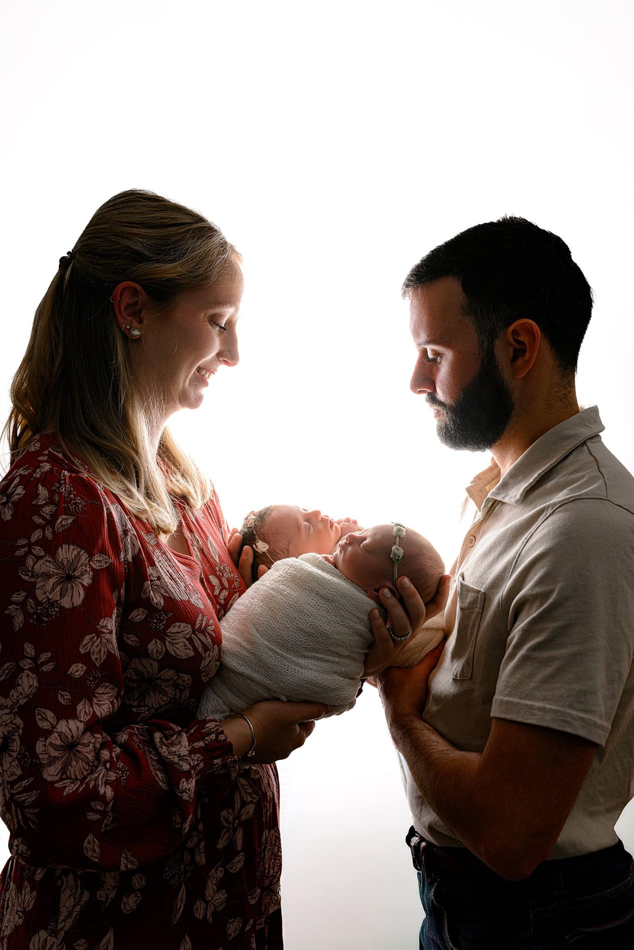 parents holding their twin newborn daughters with white light behind them