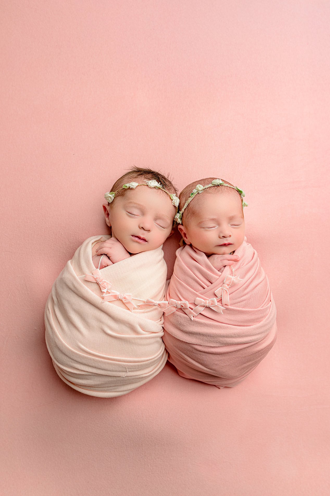 newborn twin daughters in their lifestyle newborn session wrapped in shades of pink