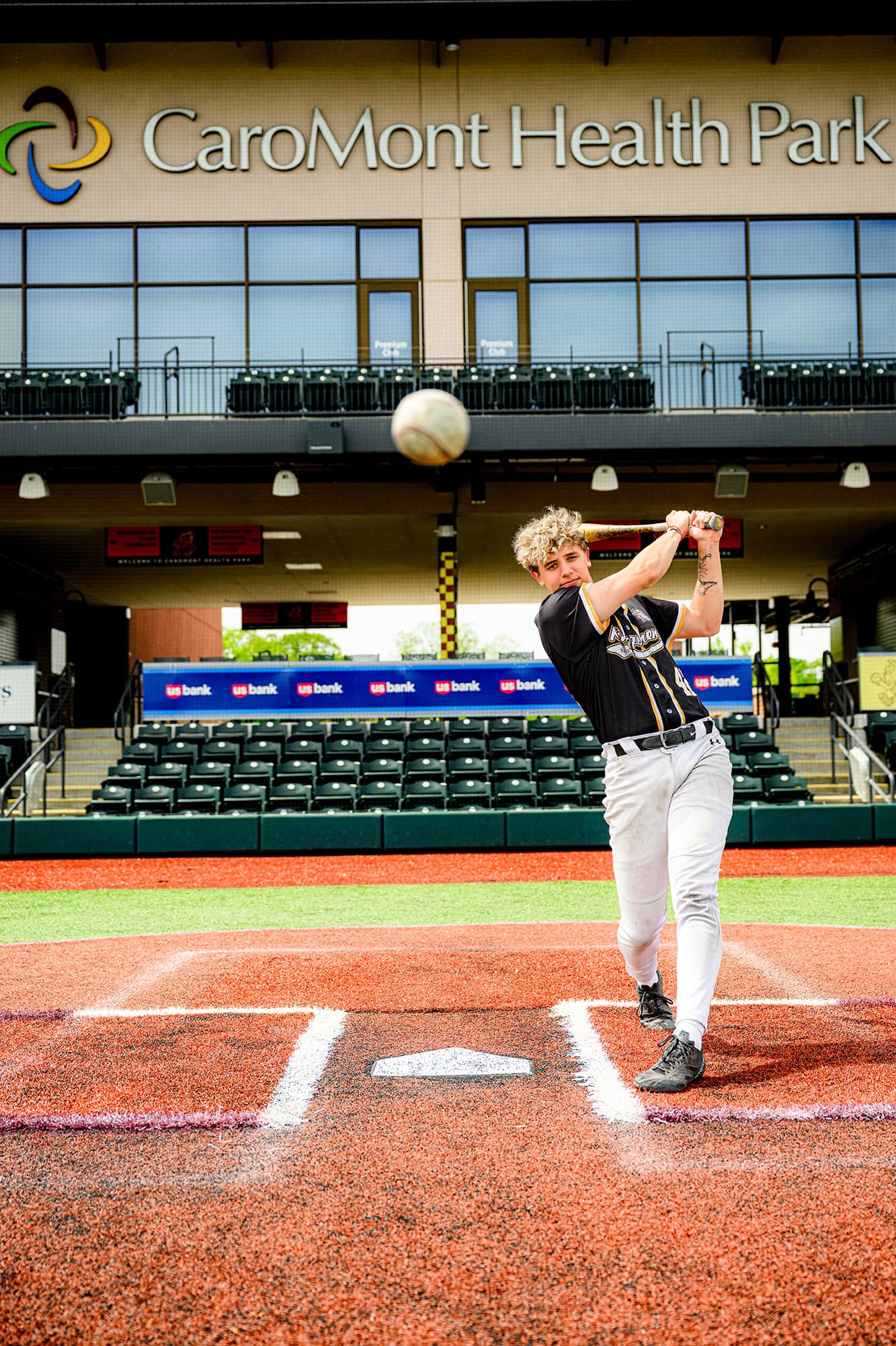charlotte senior up to bat swinging a bat while a baseball is in the foreground for his senior portraits