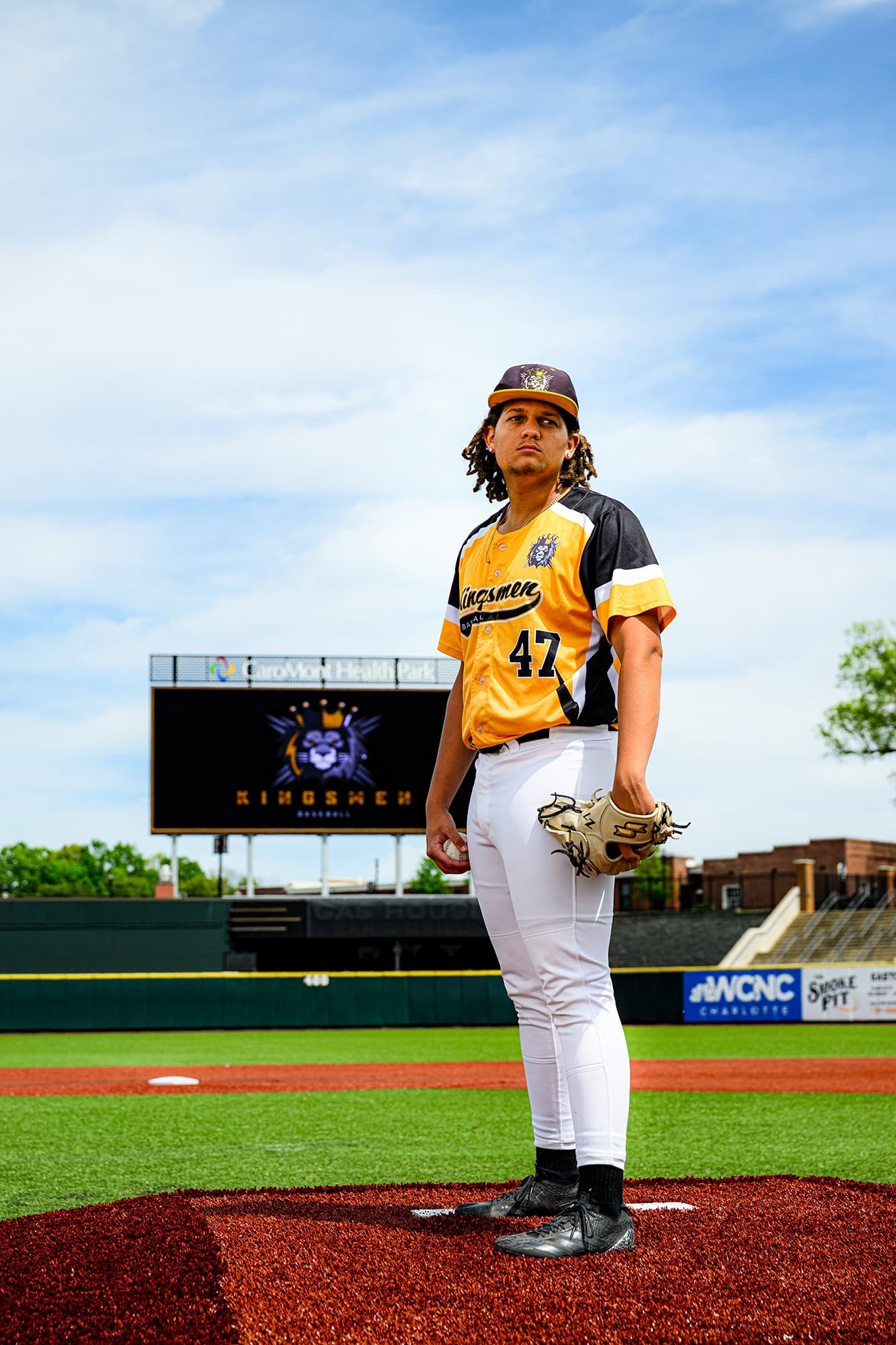 pitcher on the mound watching home with kingsmen academy logo on scoreboard behind him