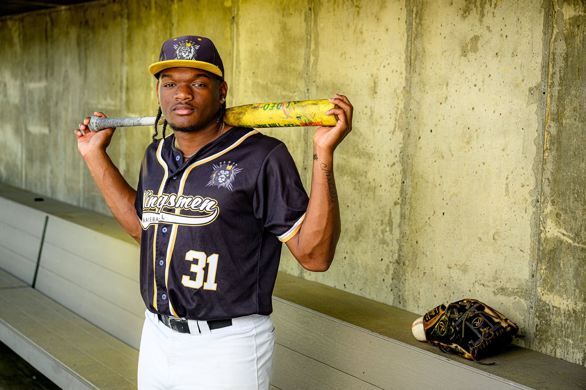 Kingsmen baseball player holding a bat in the dug out during his senior photos