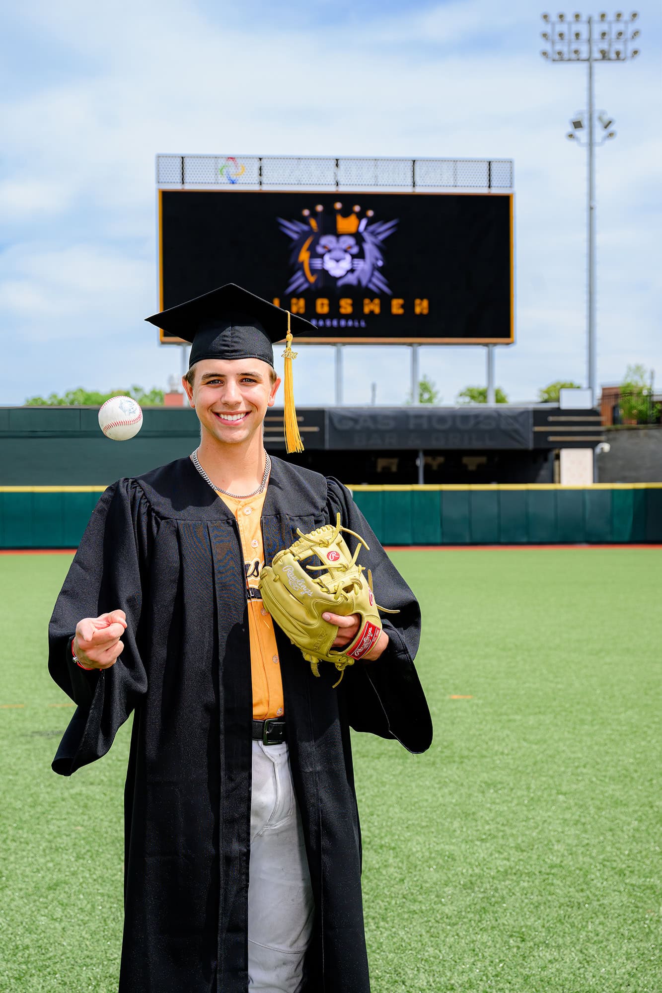charlotte senior portrait of baseball player in cap and gown with kingsmen academy logo on scoreboard behind him