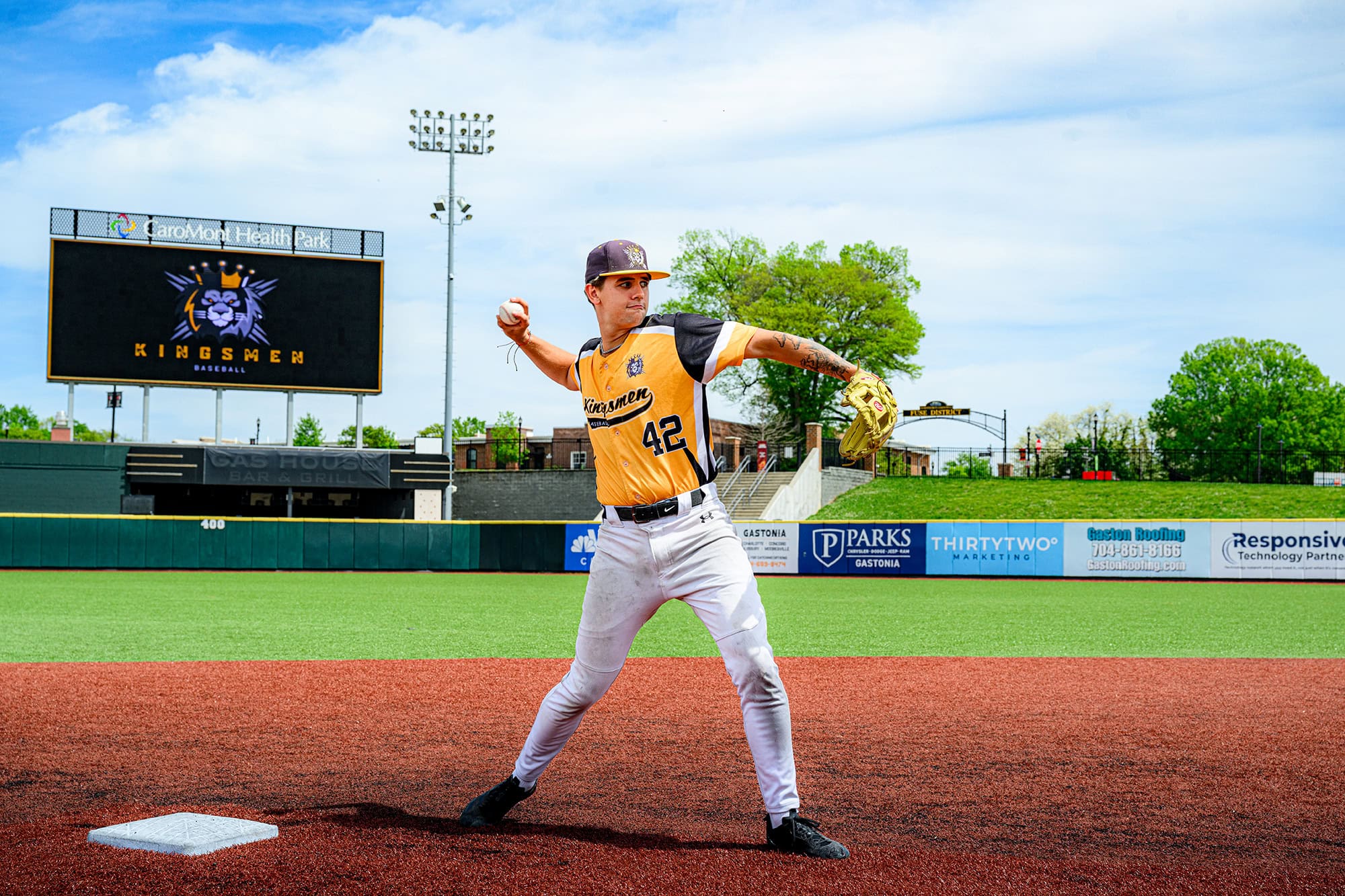 Short stop throw to first image of Kingsmen baseball player with screen in the background with the kingsmen logo