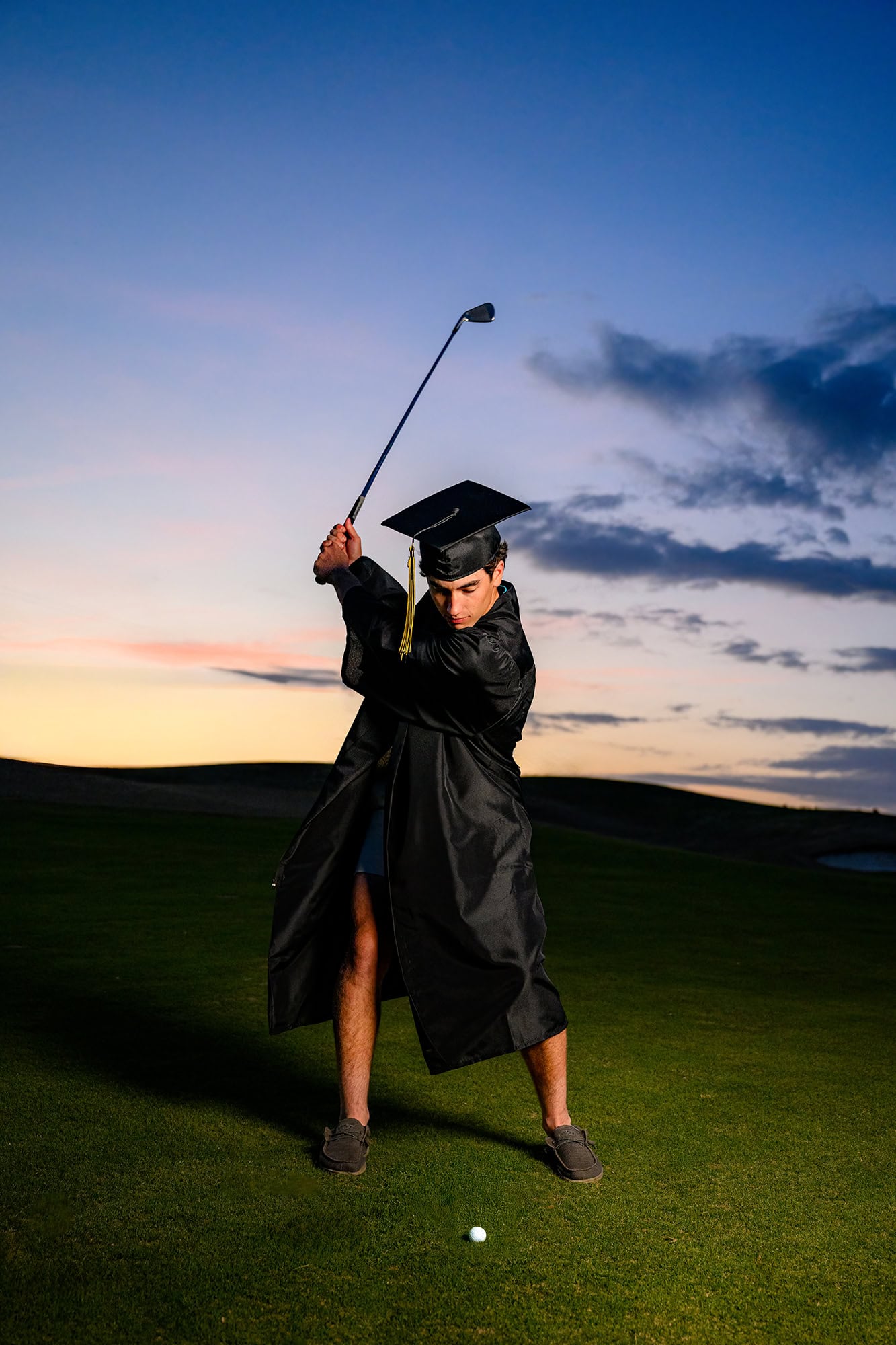 senior standing on golf course swinging a golf club wearing a cap and gown