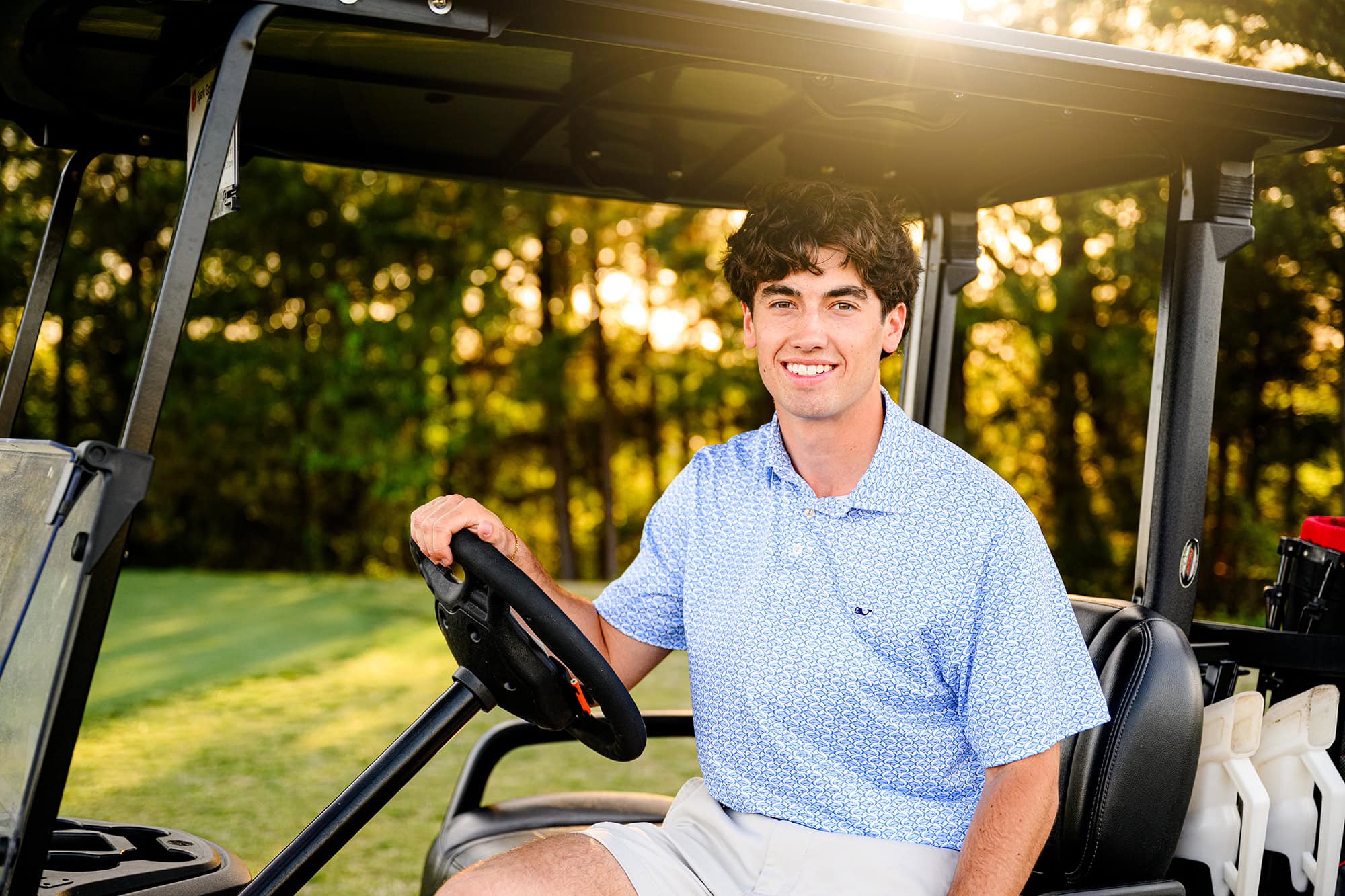 Charlotte area senior sits in golf cart wearing a blue shirt and shorts on a golf course in south carolina