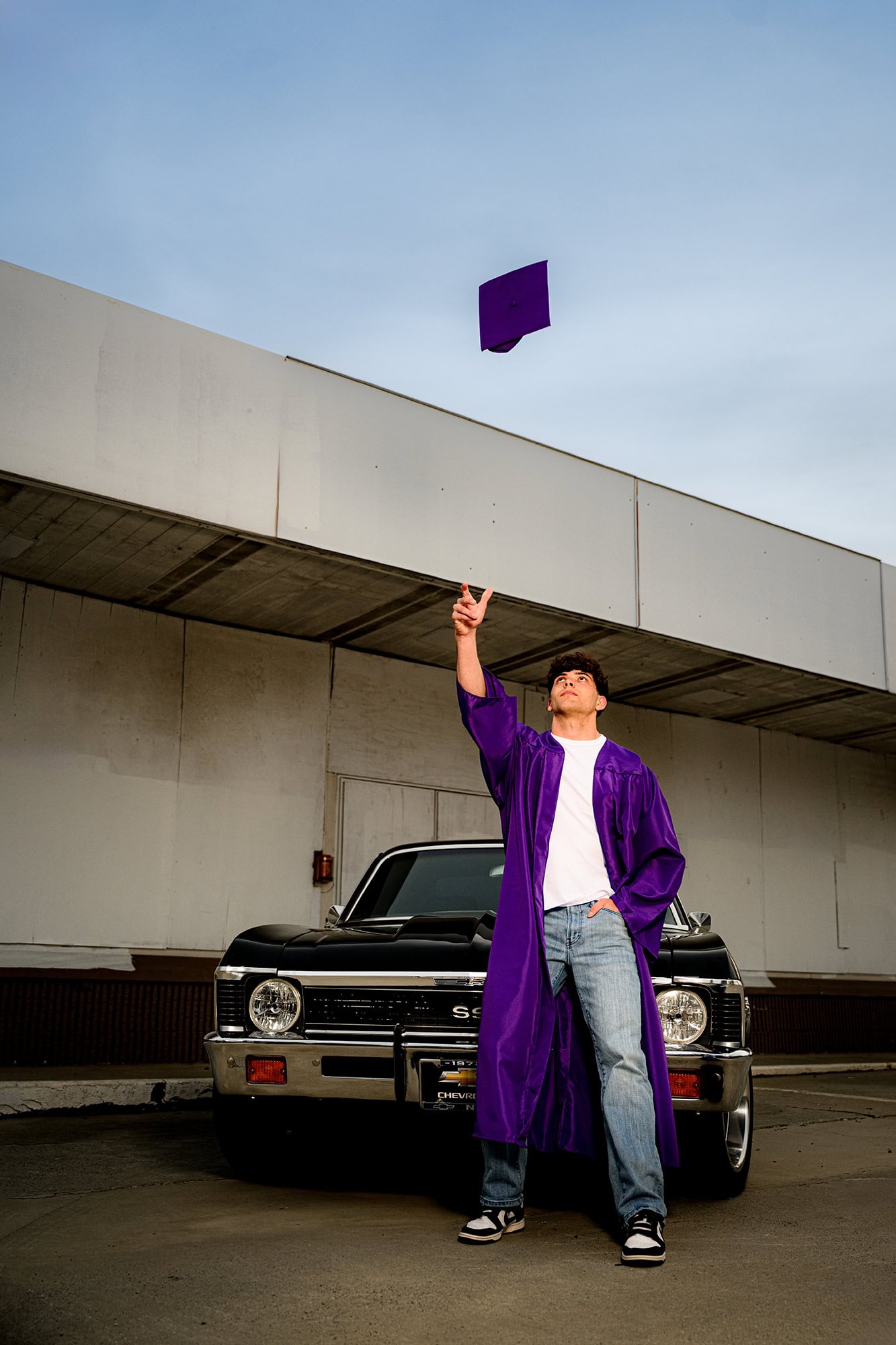 porter ridge senior tossing his cap while leaning against a black classic car for his grad photos