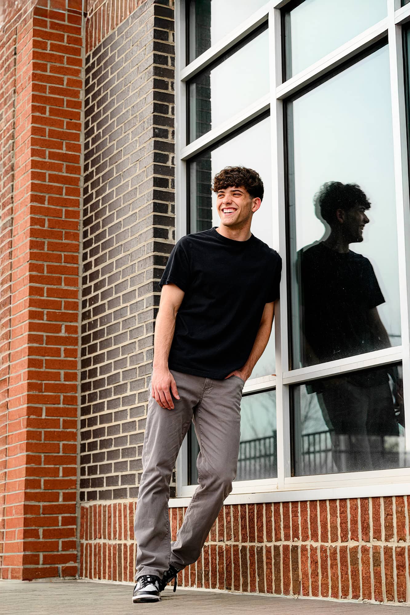 charlotte senior wearing jeans and black shirt leaning against a glass window wall for his grad photos