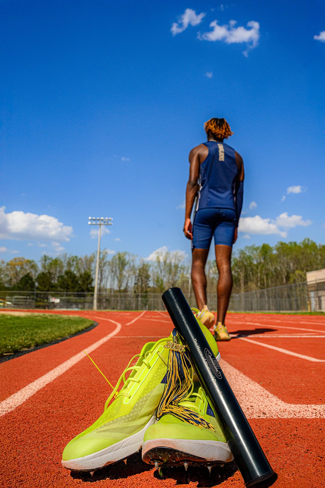 Track and Field Senior Session in Charlotte at cuthbertson stadium with shoes and batton and graduation tassel in forefront
