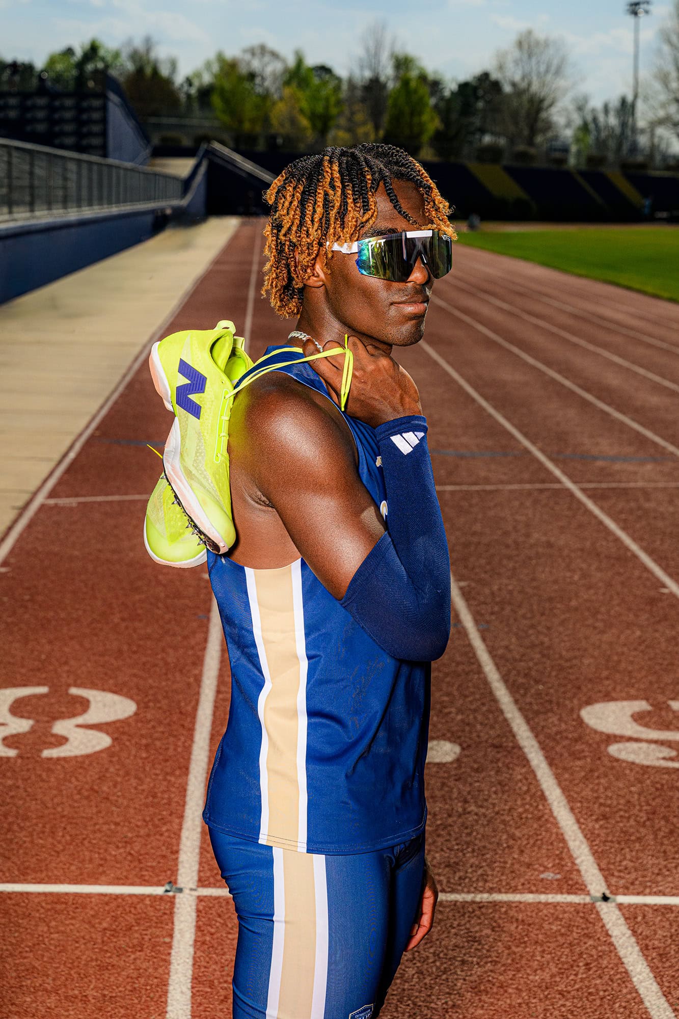 track and field athlete holds his shoes on his shoulder wearing sunglasses or his senior photos