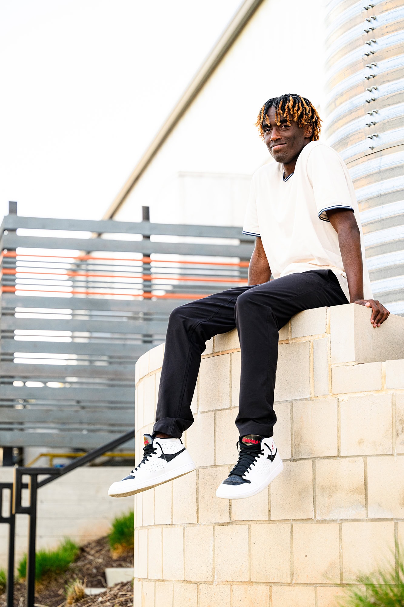 senior portrait of charlotte grad wearing a white shirt and pants sitting on a wall