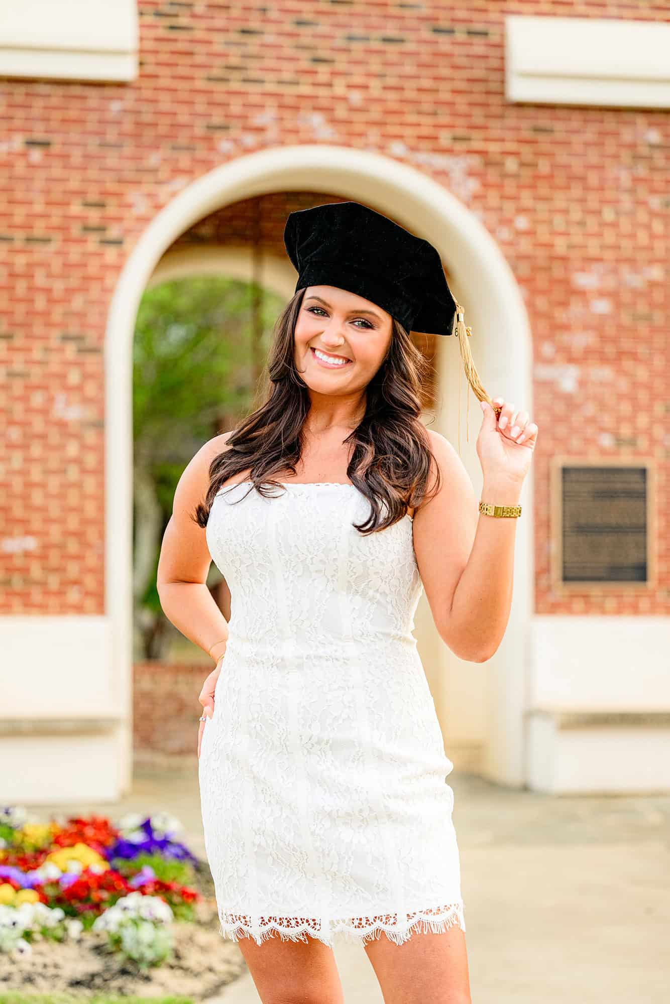 dark hair wingate university grad wearing her cap and holding her tassel in front of the iconic bell tower
