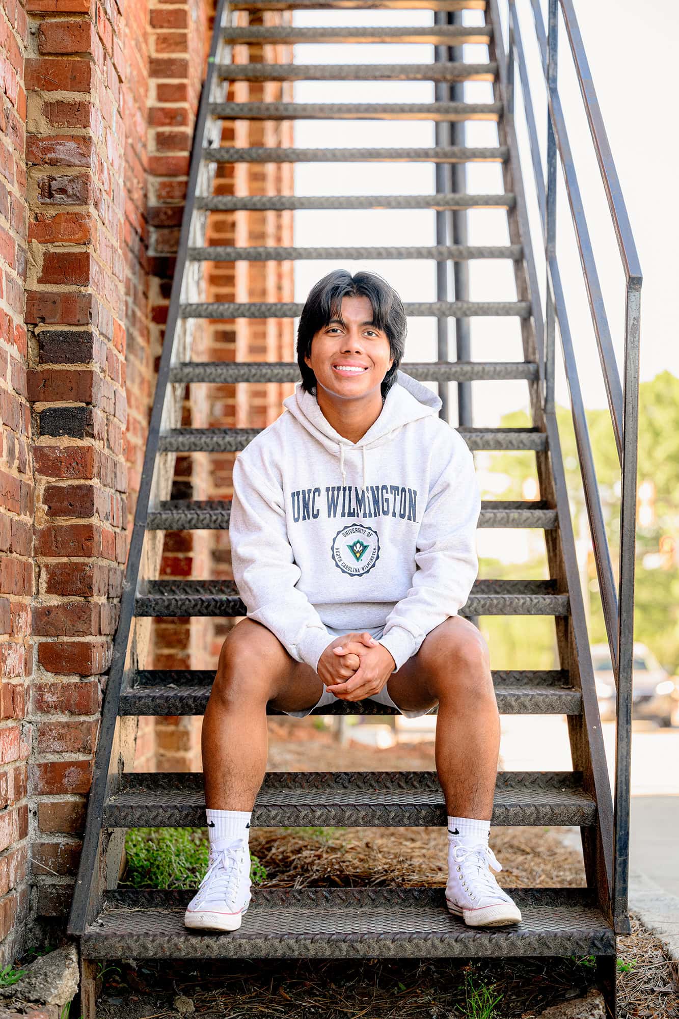 charlotte senior boy sitting on a metal staircase wearing his college gear in downtown waxhaw