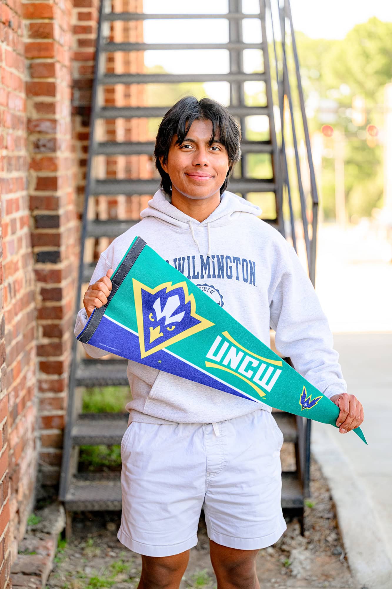 senior boy holding UNC Wilmington pennant wearing a college sweatshirt