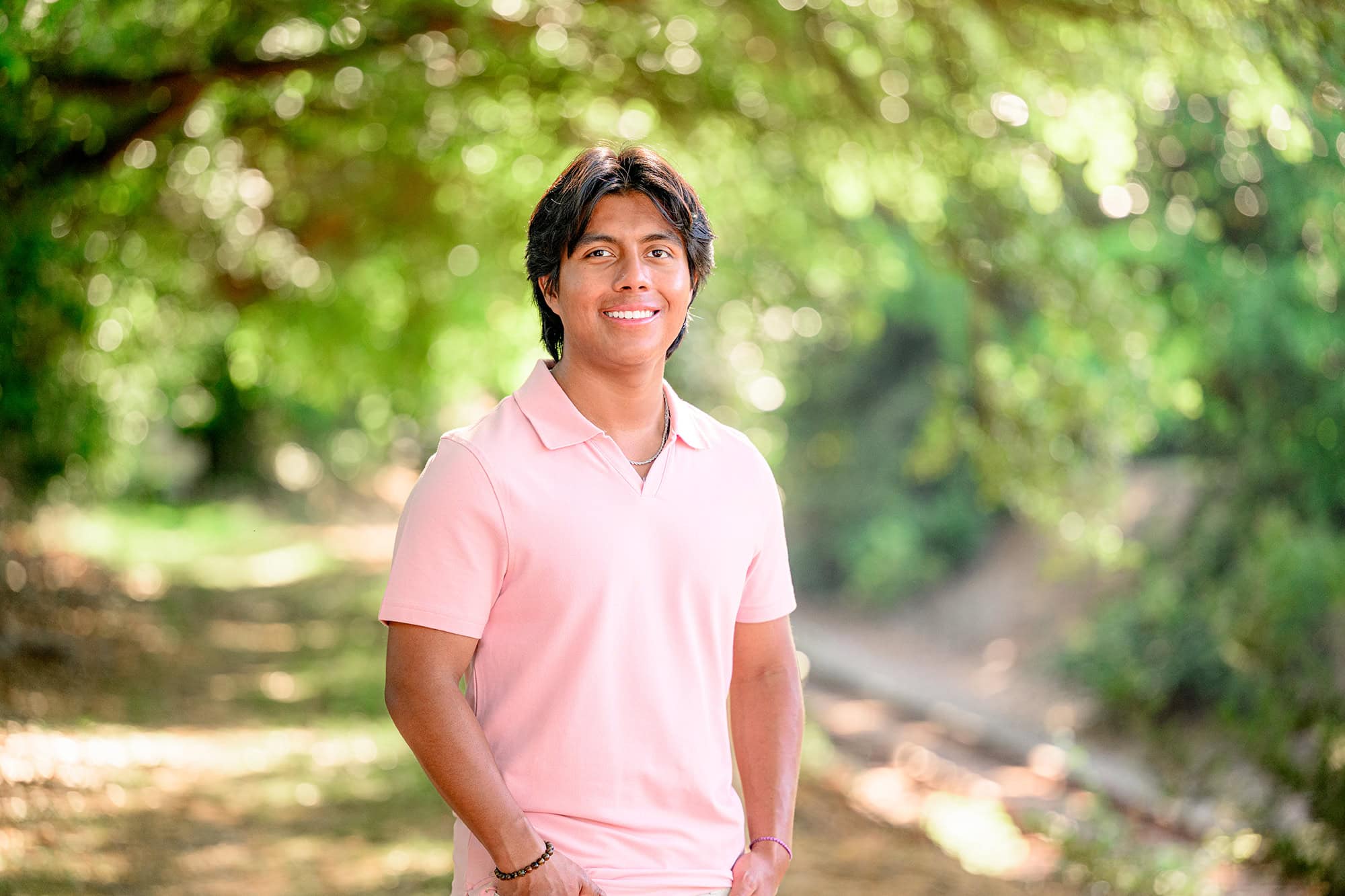 senior boy standing in the morning light wearing a pink shirt