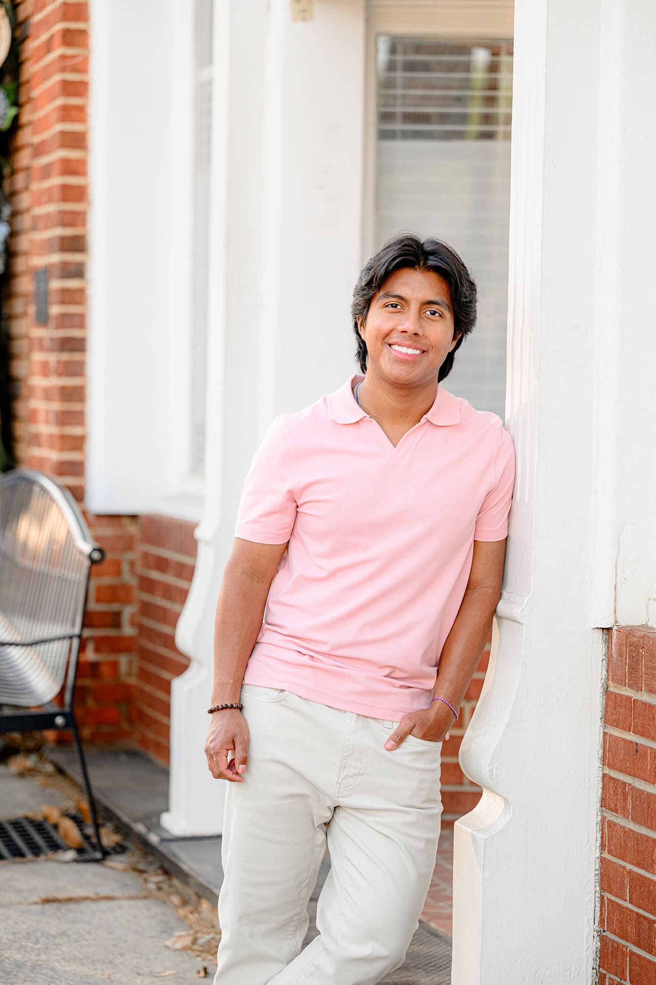 senior boy with his hand in his pocket leaning against a column in downtown waxhaw in the morning
