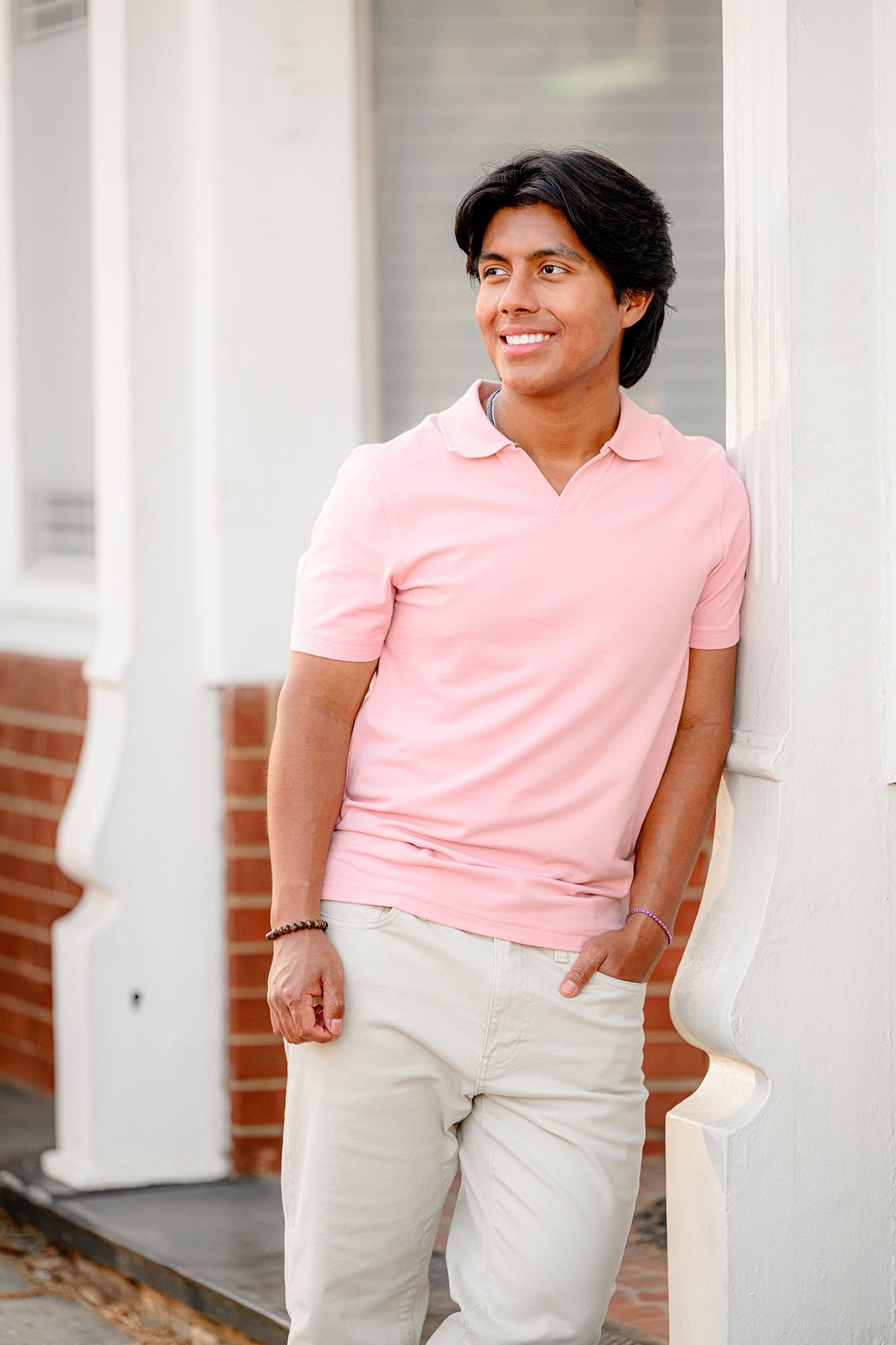 senior boy leans against wall in downtown waxhaw wearing a pink shirt