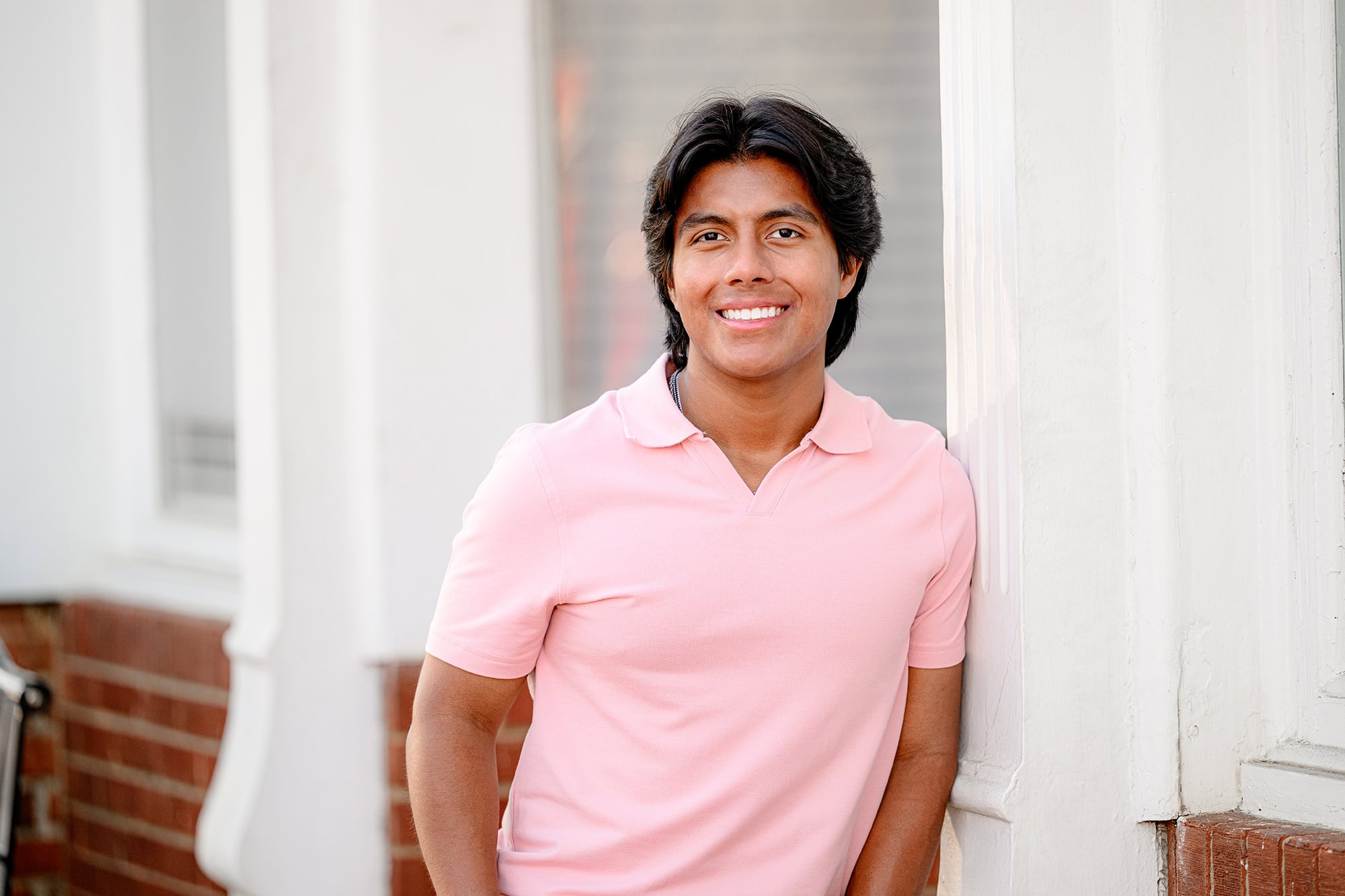 dark hair senior boy wearing light pink shirt leaning against a wall in downtown waxhaw