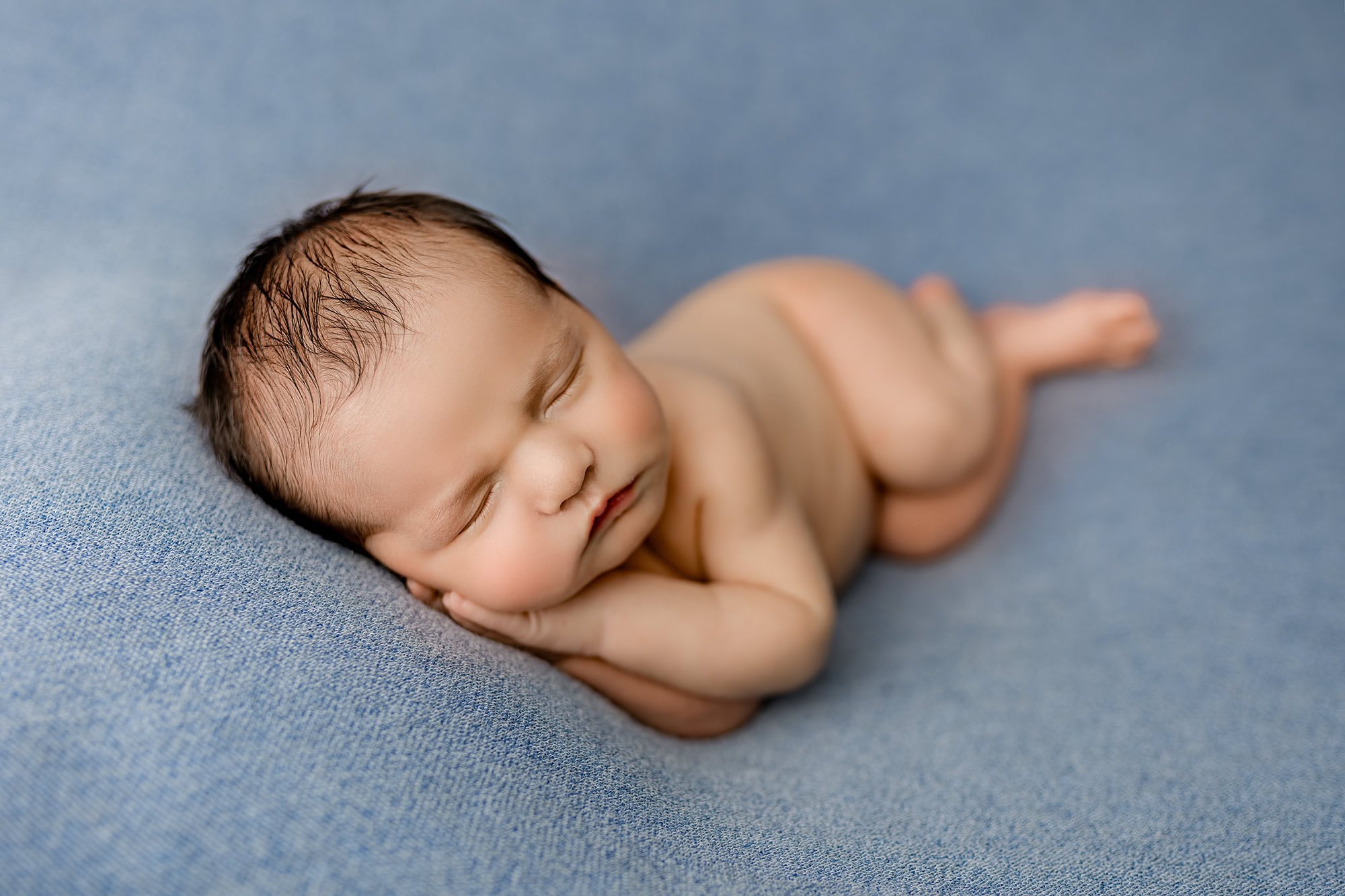 newborn baby boy laying on his side posed with his hands under his cheeks