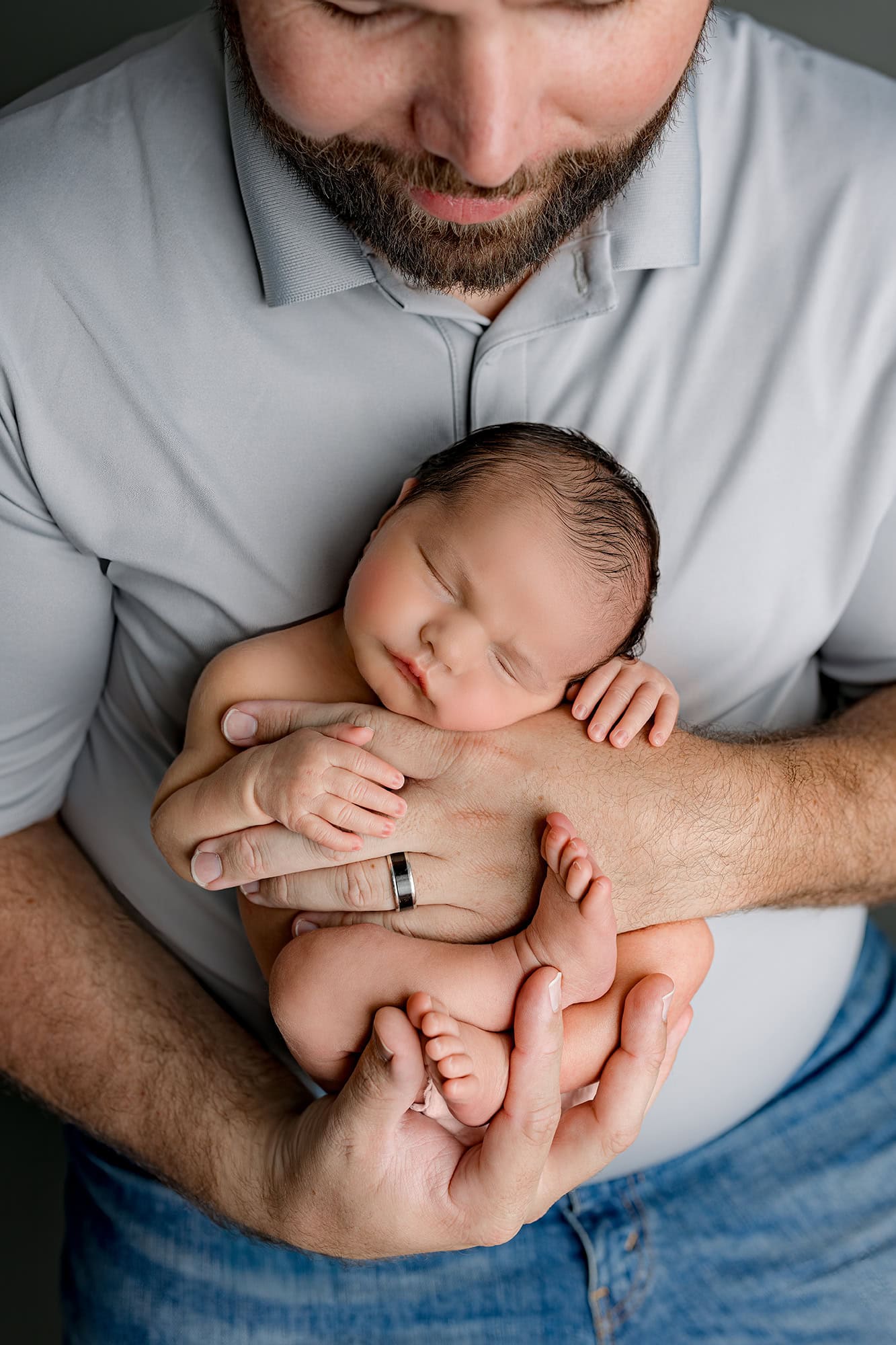 dad holding newborn son in his arms posed where you can see baby's tiny features compared to dad's hands