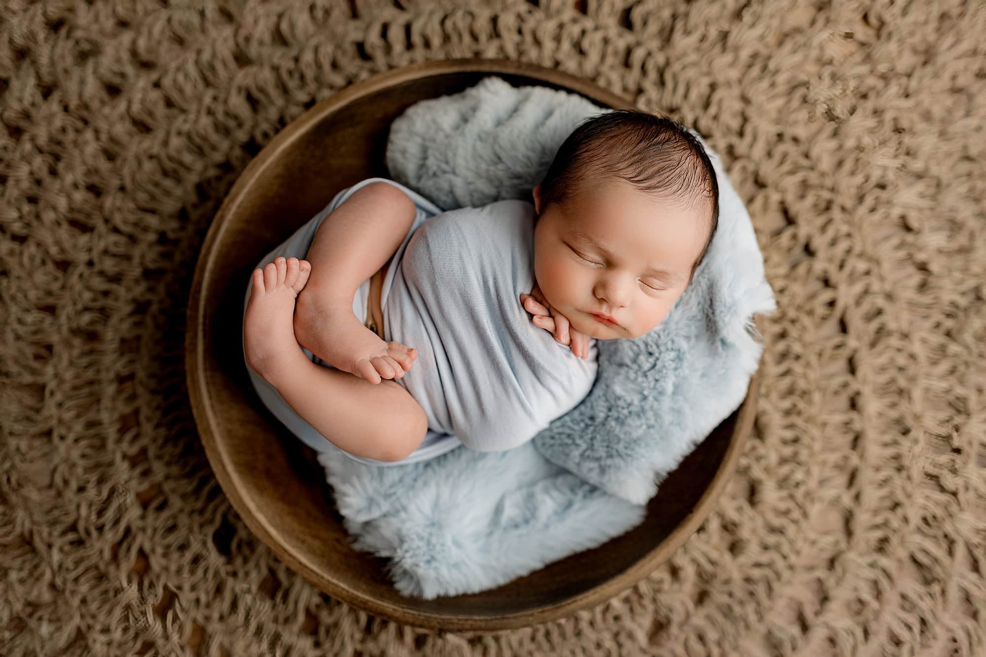 baby posed in a bowl wrapped in a blue wrap