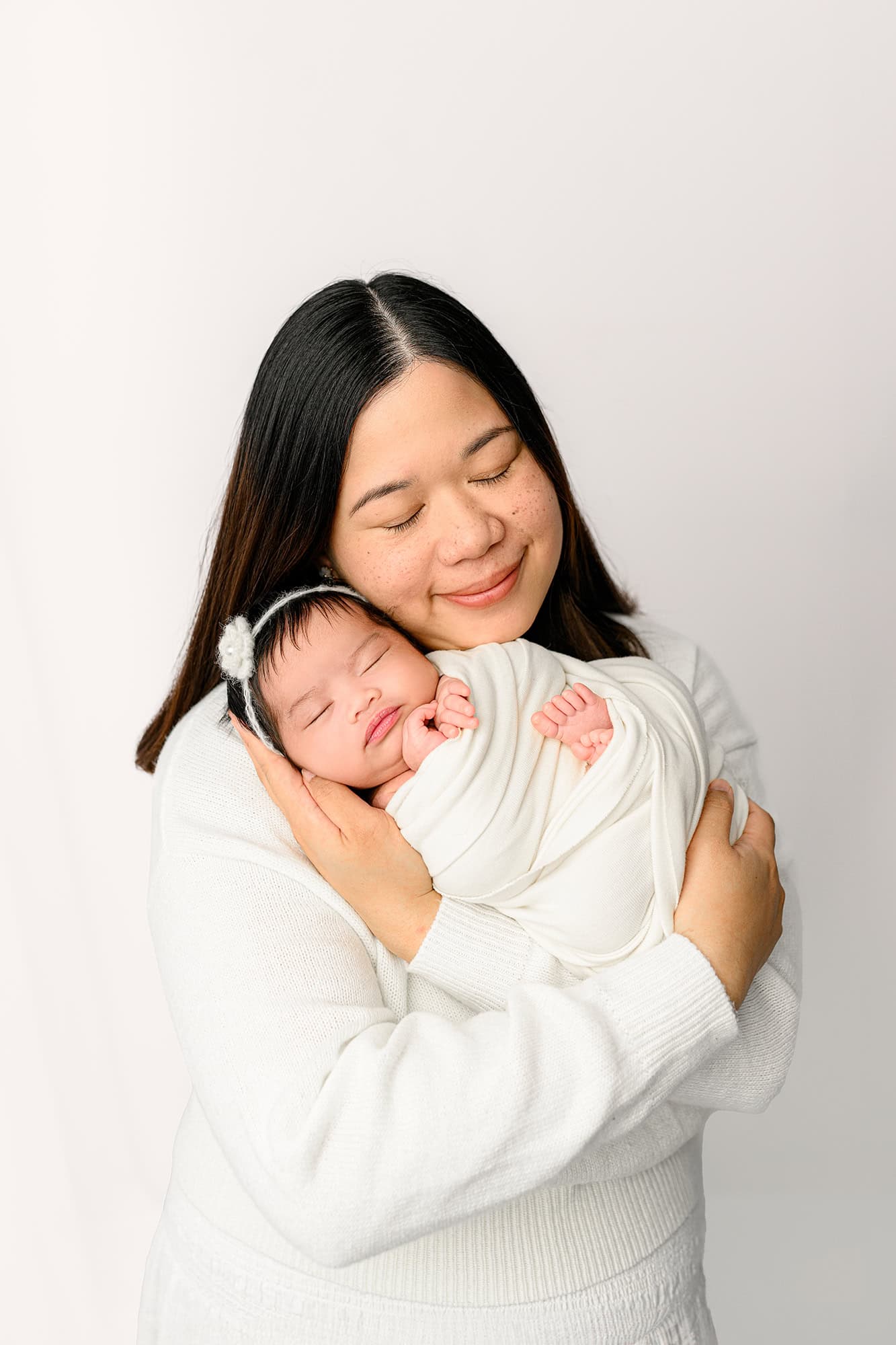 Mom holding her newborn baby girl in a white studio setting after having a neutral themed baby shower