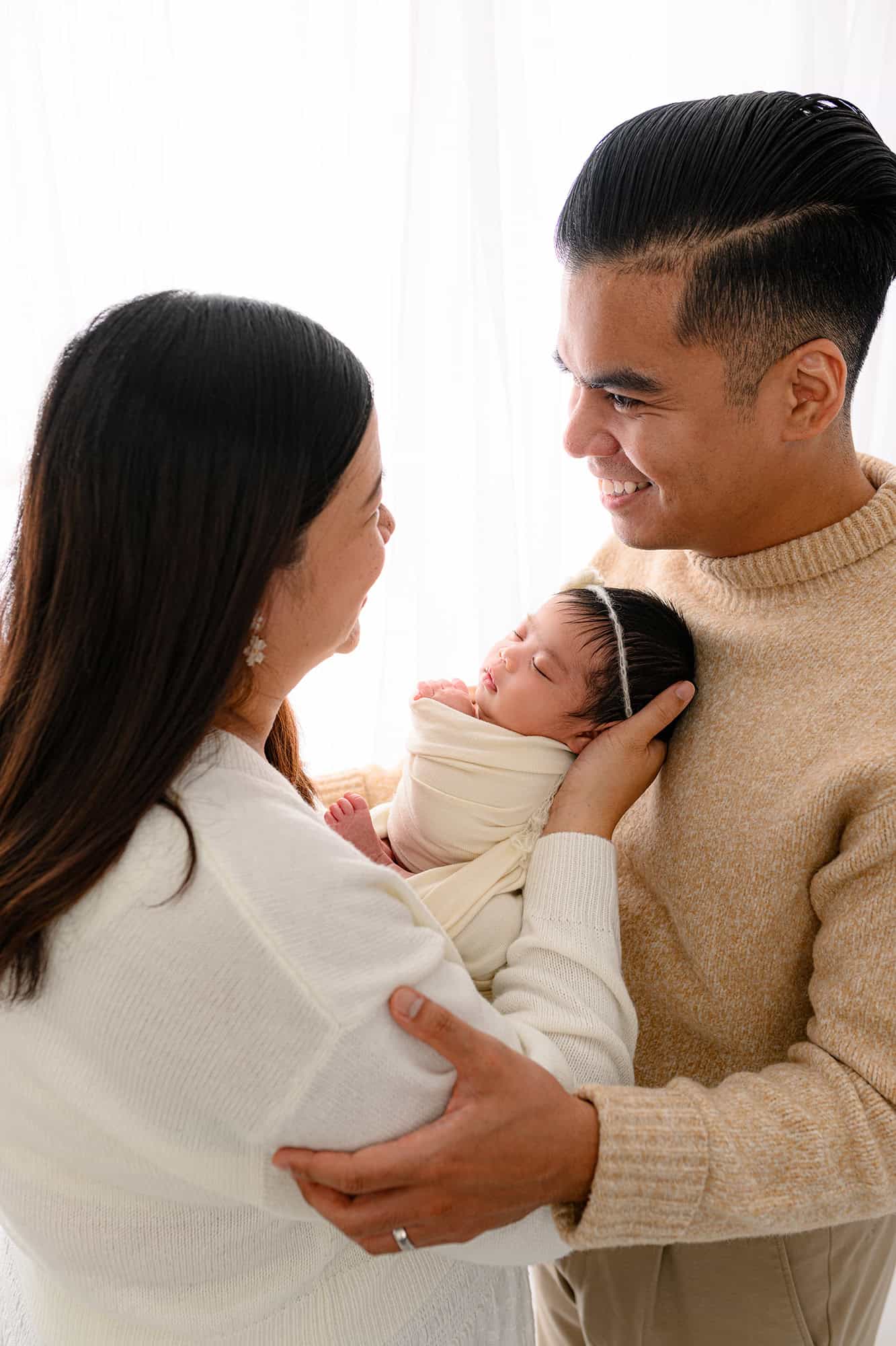 Couple standing together holding their brand new baby in an all white set up