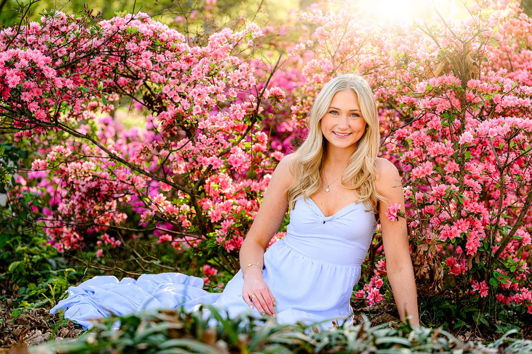 Blonde, Charlotte Catholic graduate wearing blue dress, sitting amongst azaleas.