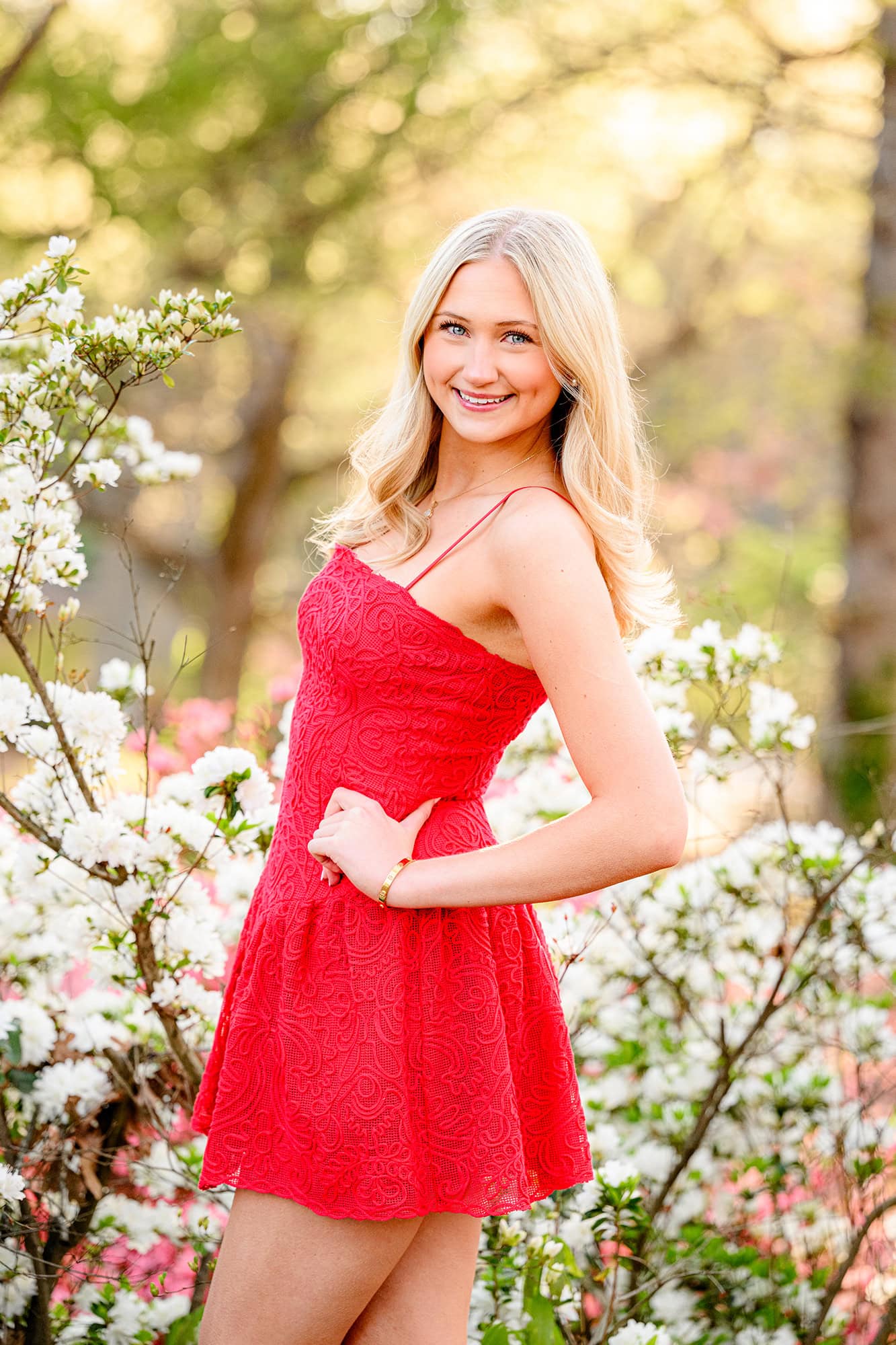 charlotte catholic graduate wearing a red dress standing in front of white azalea bush