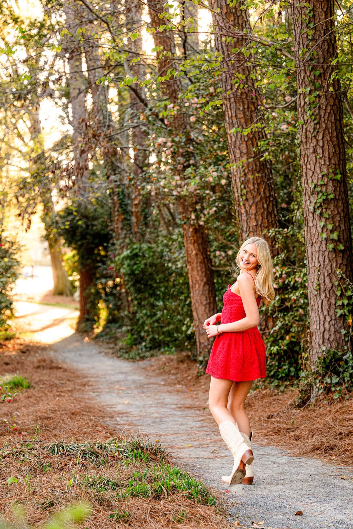 charlotte catholic grad looks back over her shoulder while wearing a red dress and boots for senior photos