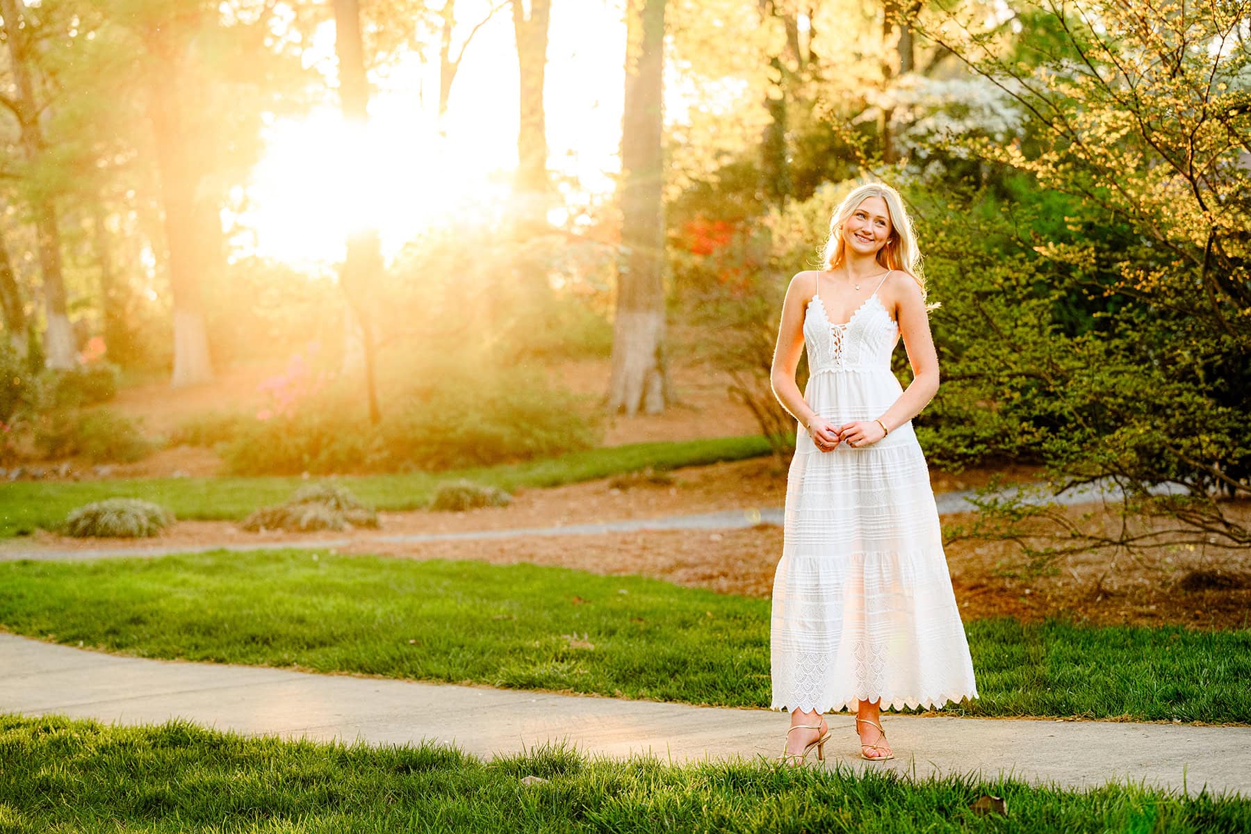 Charlotte Catholic graduate wearing white dress with glowing sunset behind her for senior photos