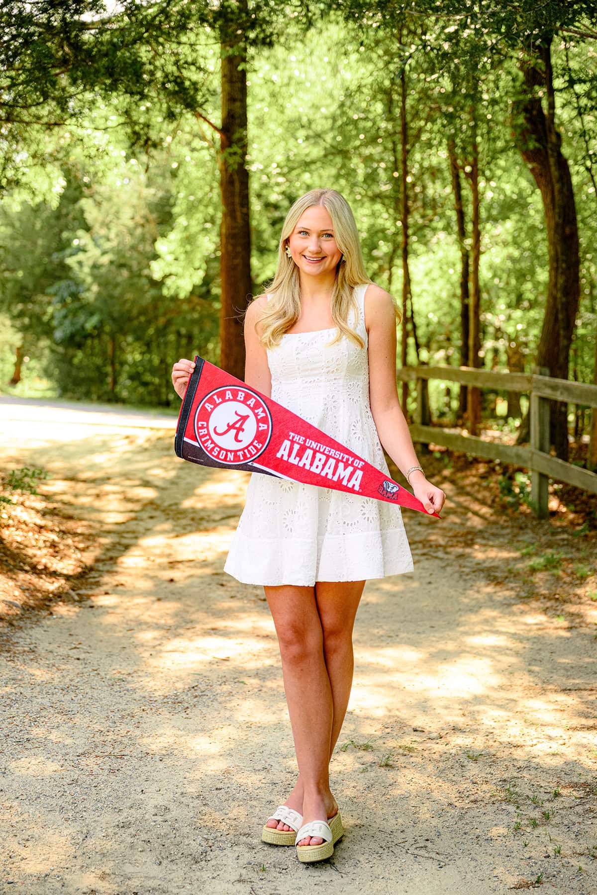 blonde charlotte catholic senior wearing white graduation dress holding her university of alabama pennant