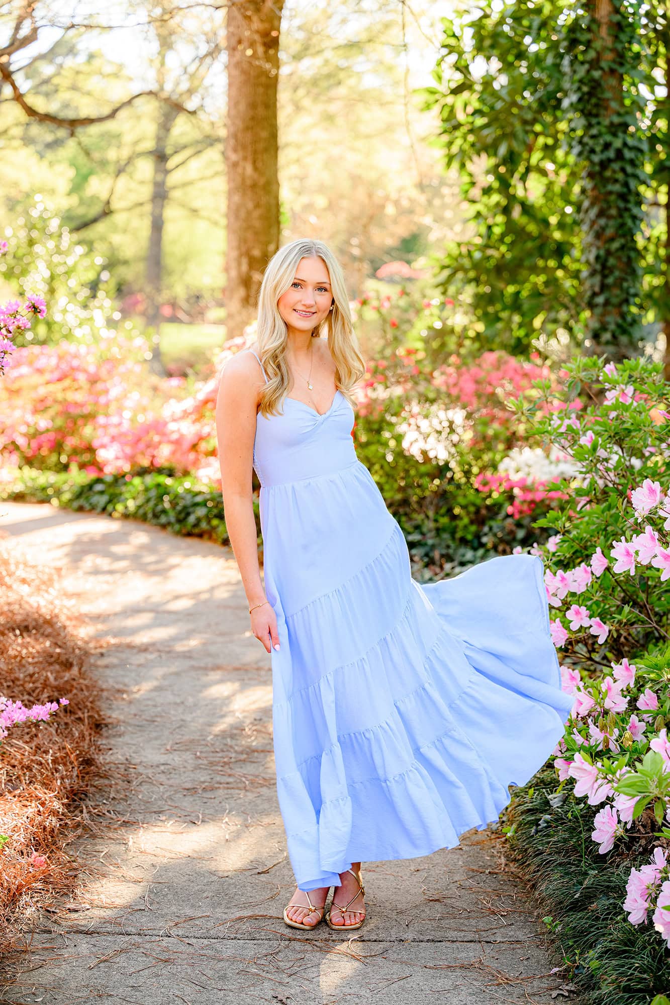 blonde charlotte catholic girl wearing blue dress standing on a pathway full of azeleas