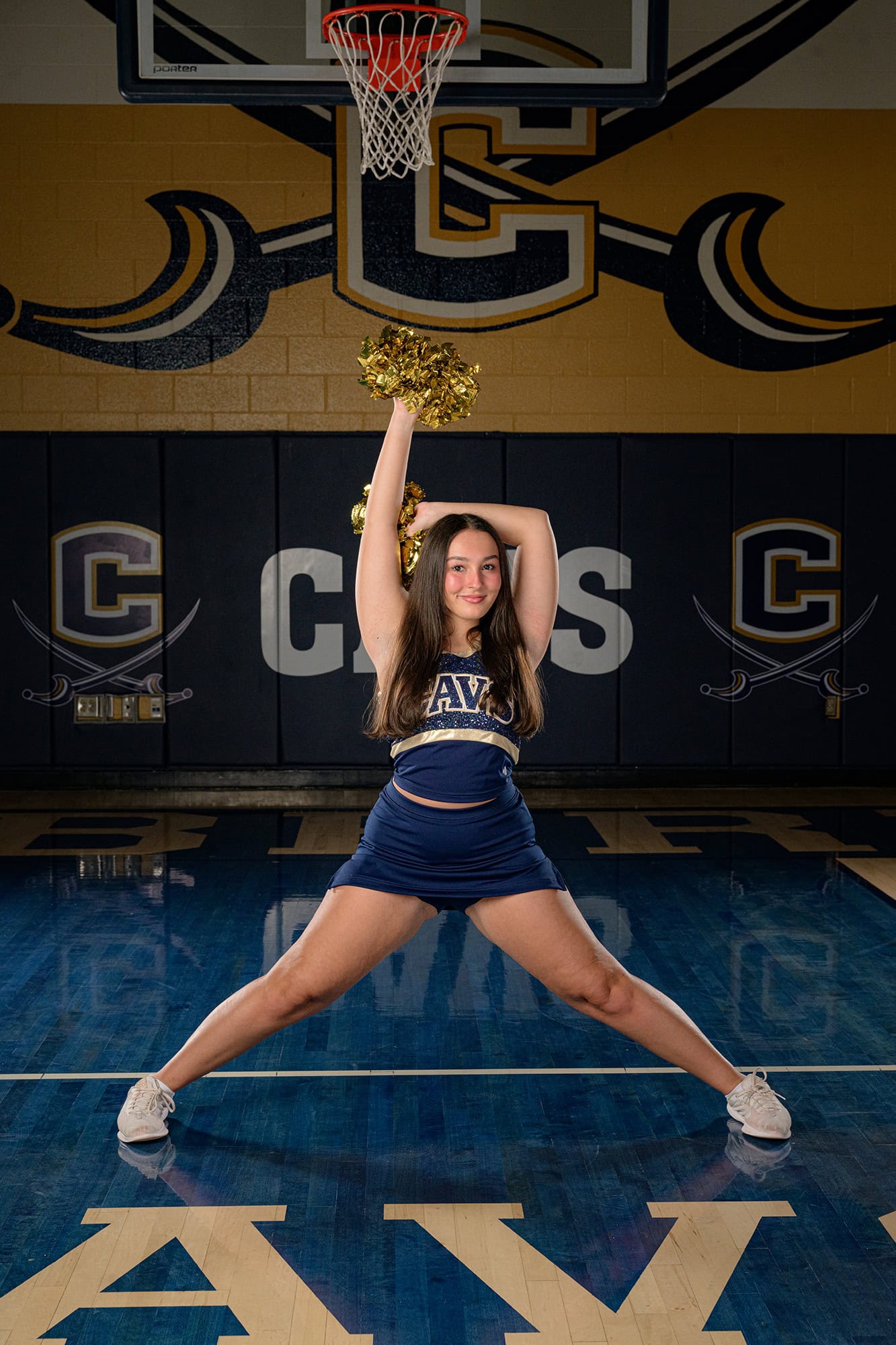 dancer posing with arm up holding pom under basketball goal