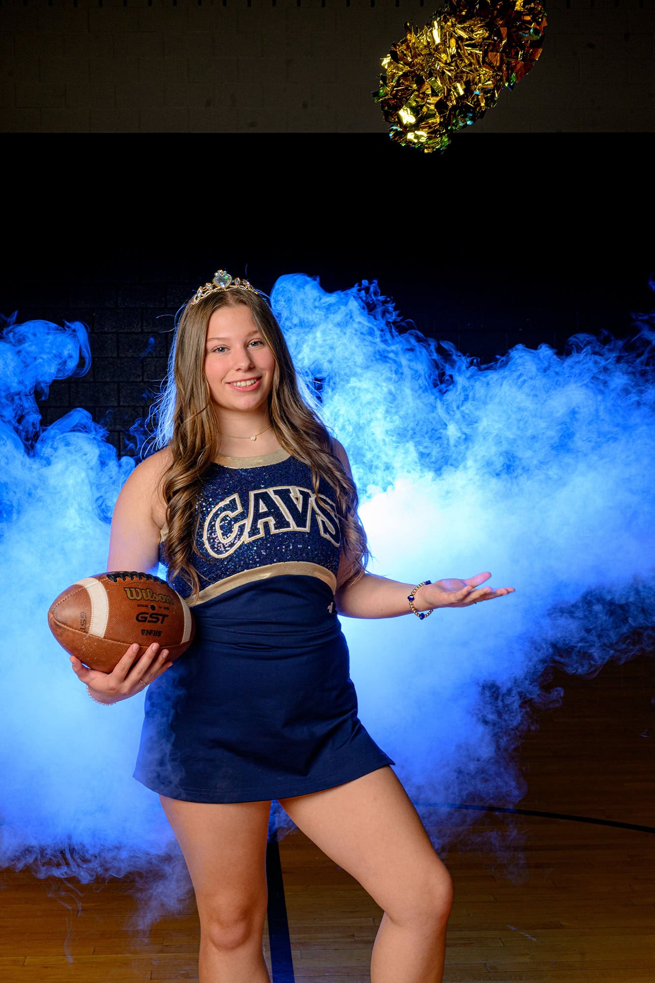 blue light behind dance team media day photo tossing pom while holding football