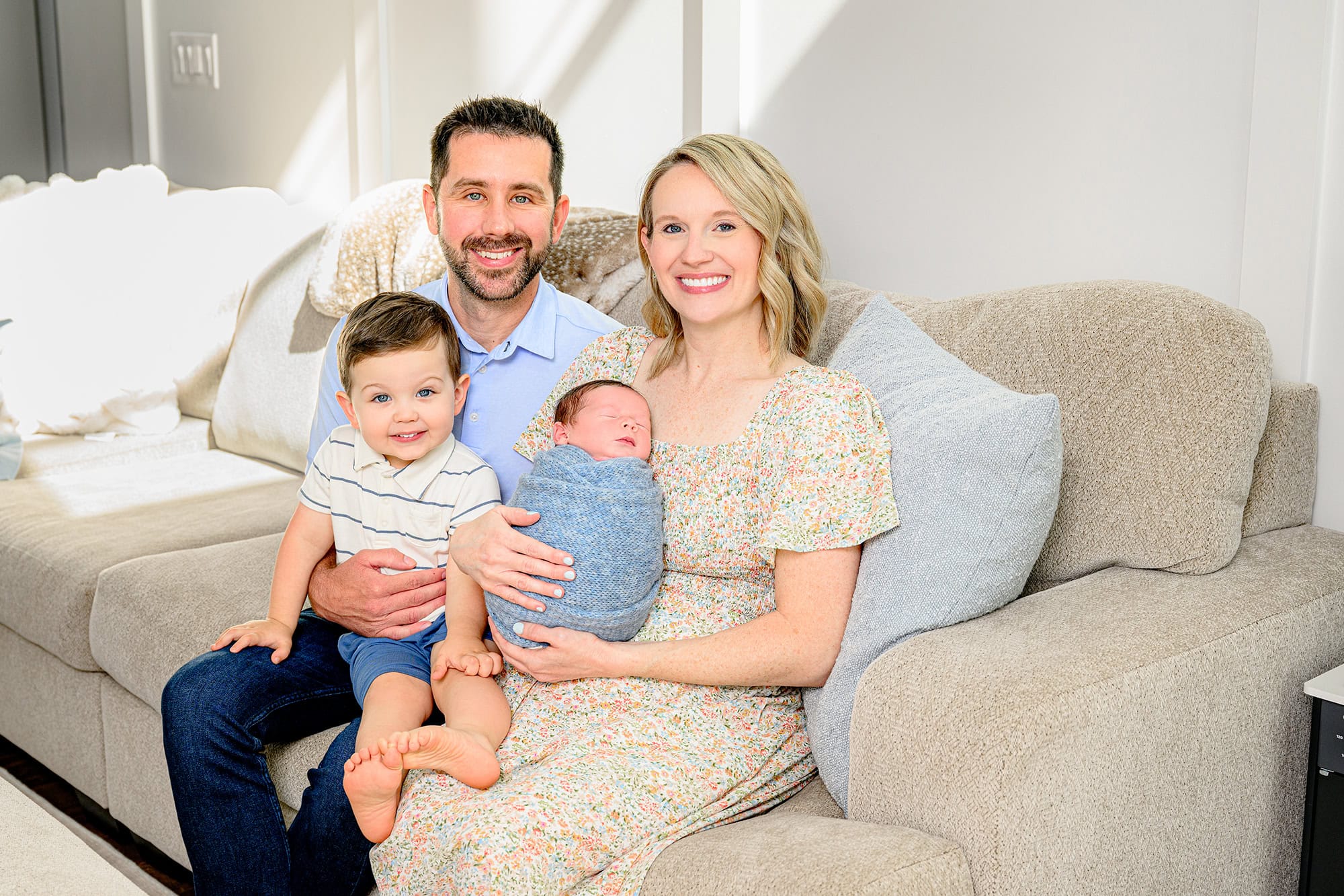 family of four sitting on their living room couch during their in home lifestyle newborn session in their charlotte area house