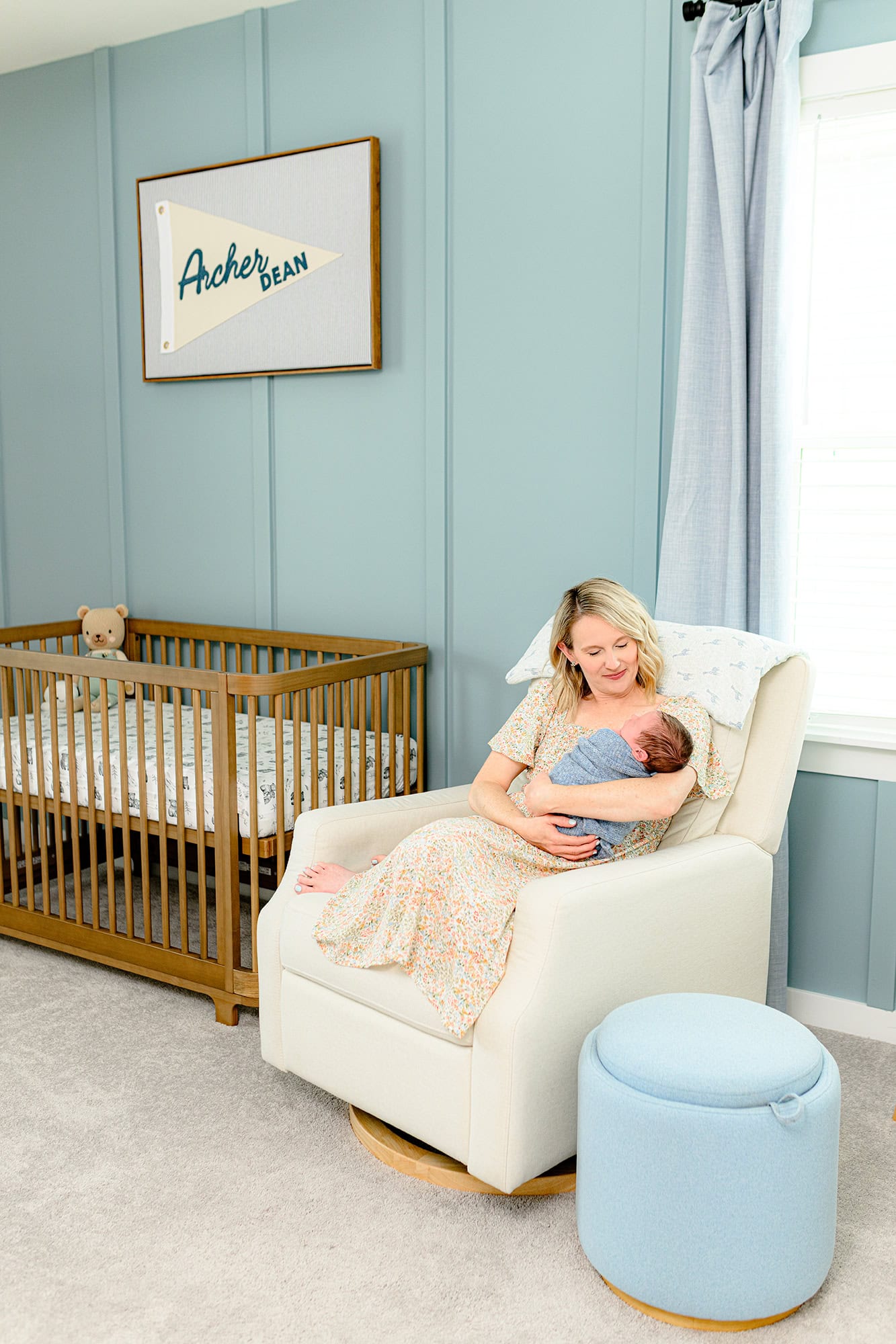 mom sitting in nursery chair holding her baby boy wrapped in blue