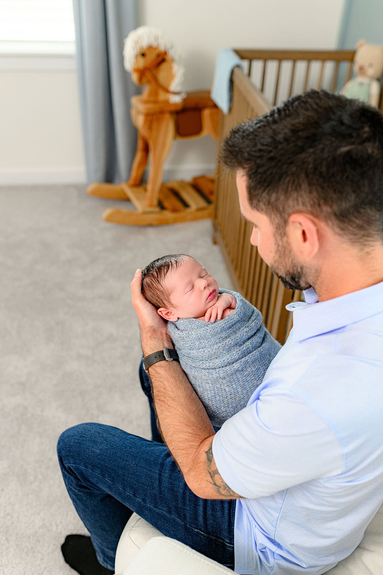 over the shoulder photo of dad holding his newborn son wrapped in blue during their in home lifestyle session