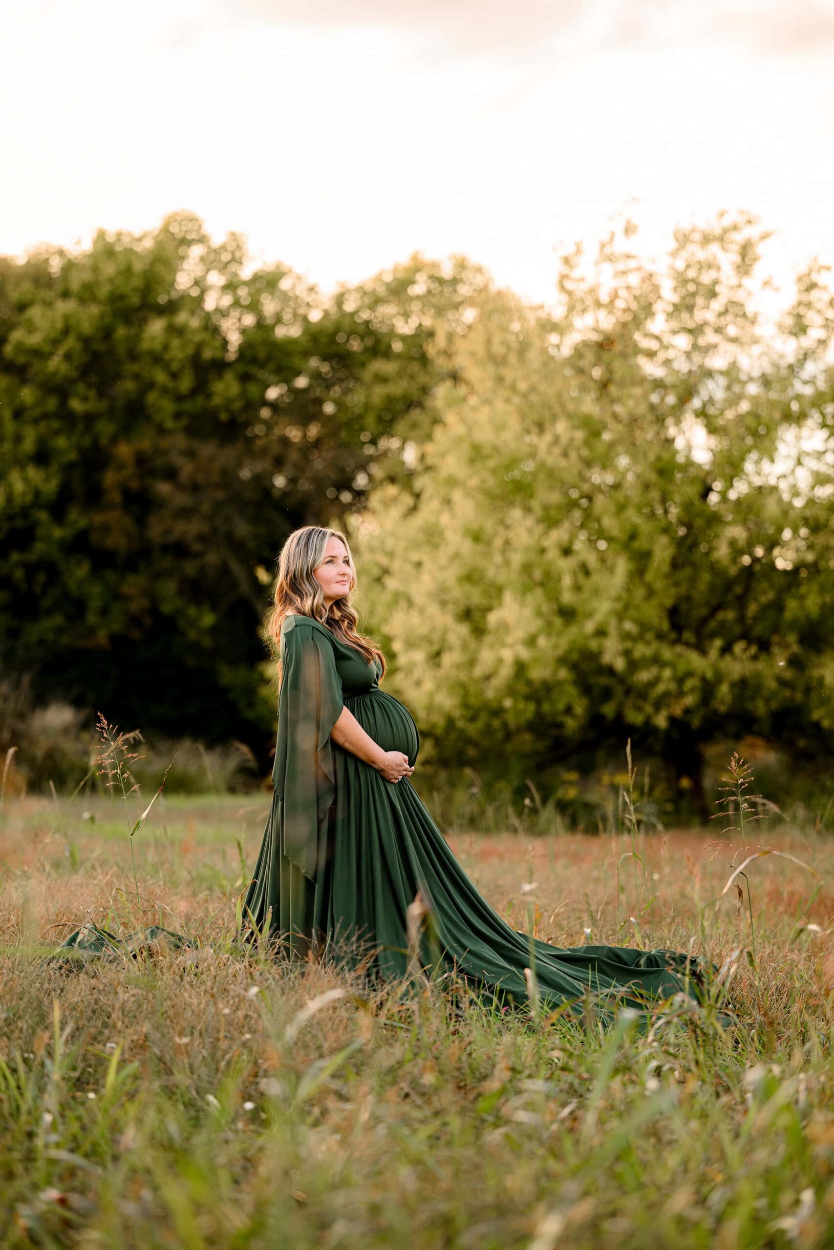 golden glow with mom to be standing in a field with green grasses behind her