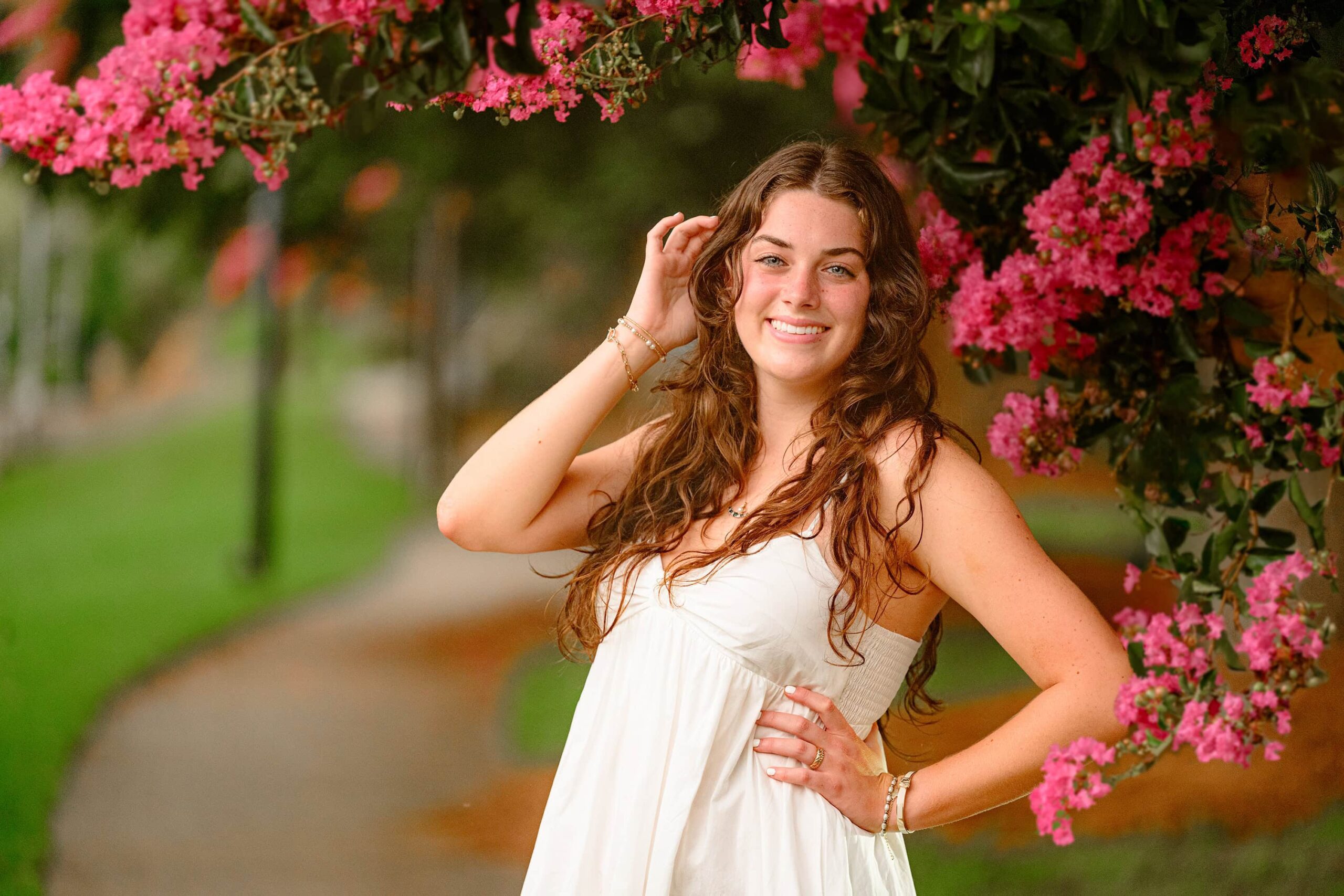 With delicate pink crape myrtle blooms surrounding her, Emma Hines gently tucks her long dark hair behind her ear, her striking green eyes standing out in this close-up senior session portrait in downtown Waxhaw.