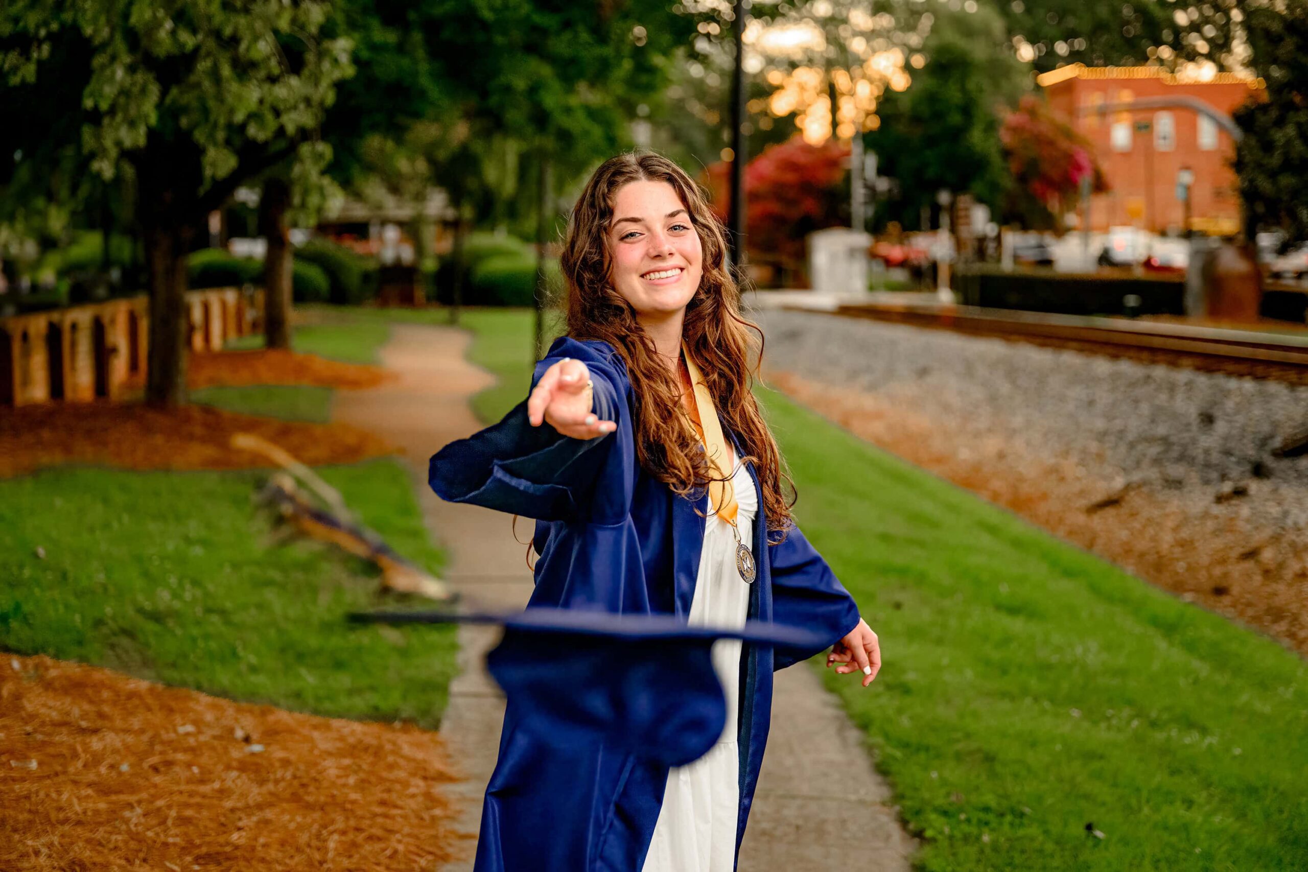 Emma Hines, a Cuthbertson High School graduate, playfully tosses her blue graduation cap like a frisbee during her senior session in downtown Waxhaw, celebrating this milestone with joy and excitement.